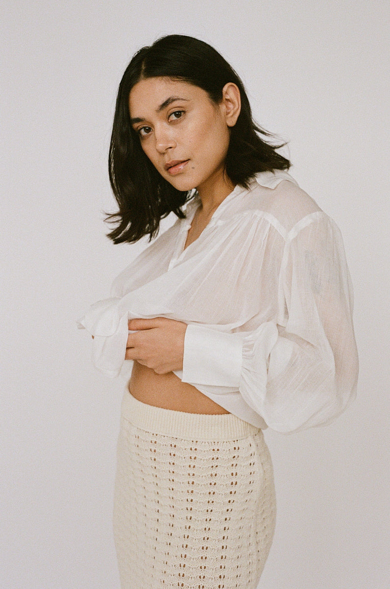 Woman in a white sheer blouse and Straight Knit Skirt - Ivory, handmade in Peru, posing against a neutral background.