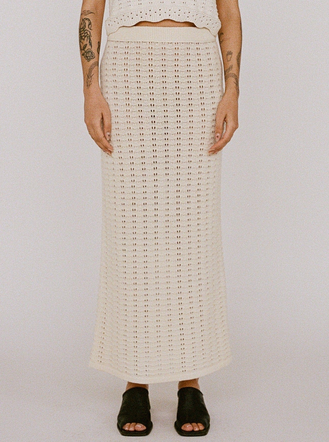 Woman standing in a 100% cotton, white crocheted top and Straight Knit Skirt - Ivory ensemble against a neutral backdrop.