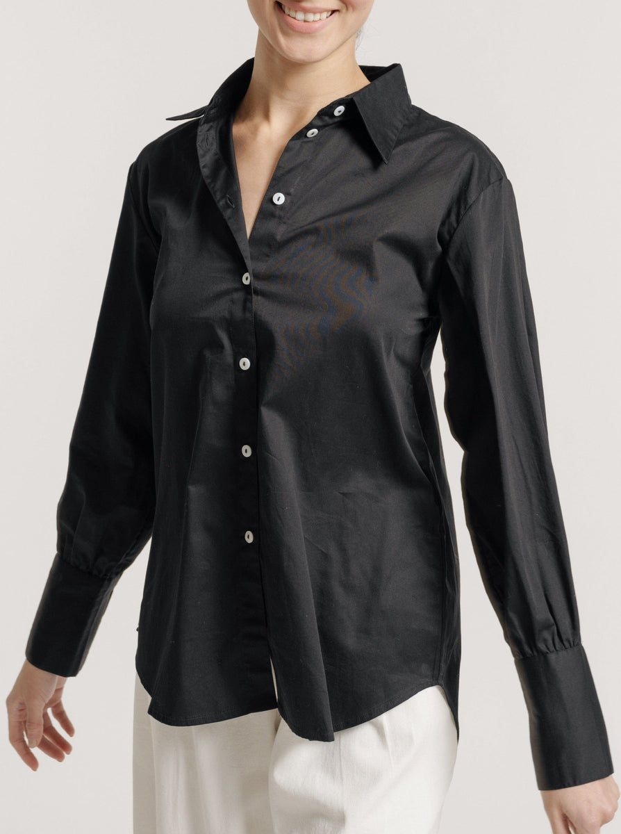 A woman wearing a Museo Button Up - Black organic cotton shirt and white pants.