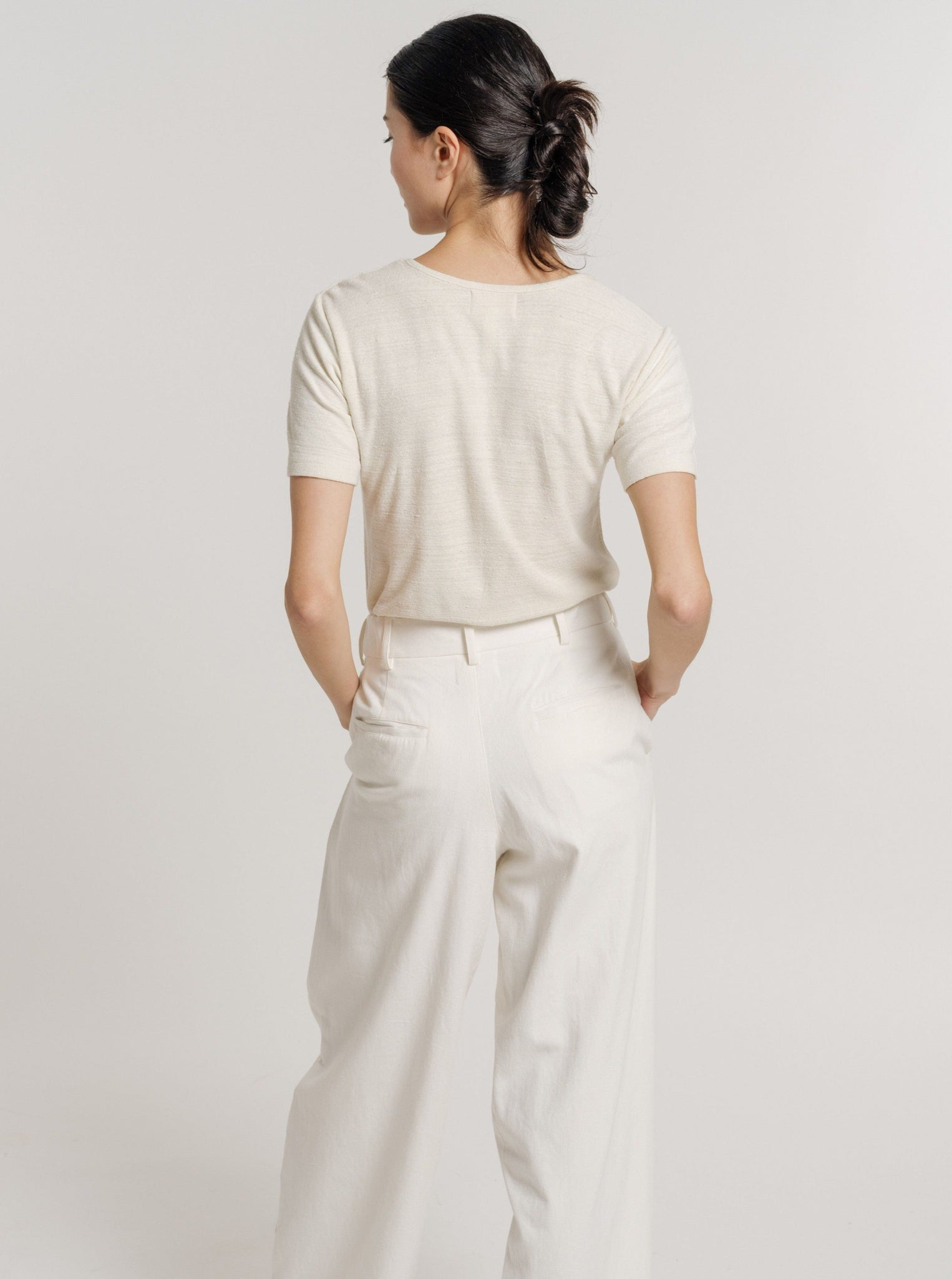 The back view of a woman wearing a Baby Tee - Ivory - pre-order and wide leg pants.