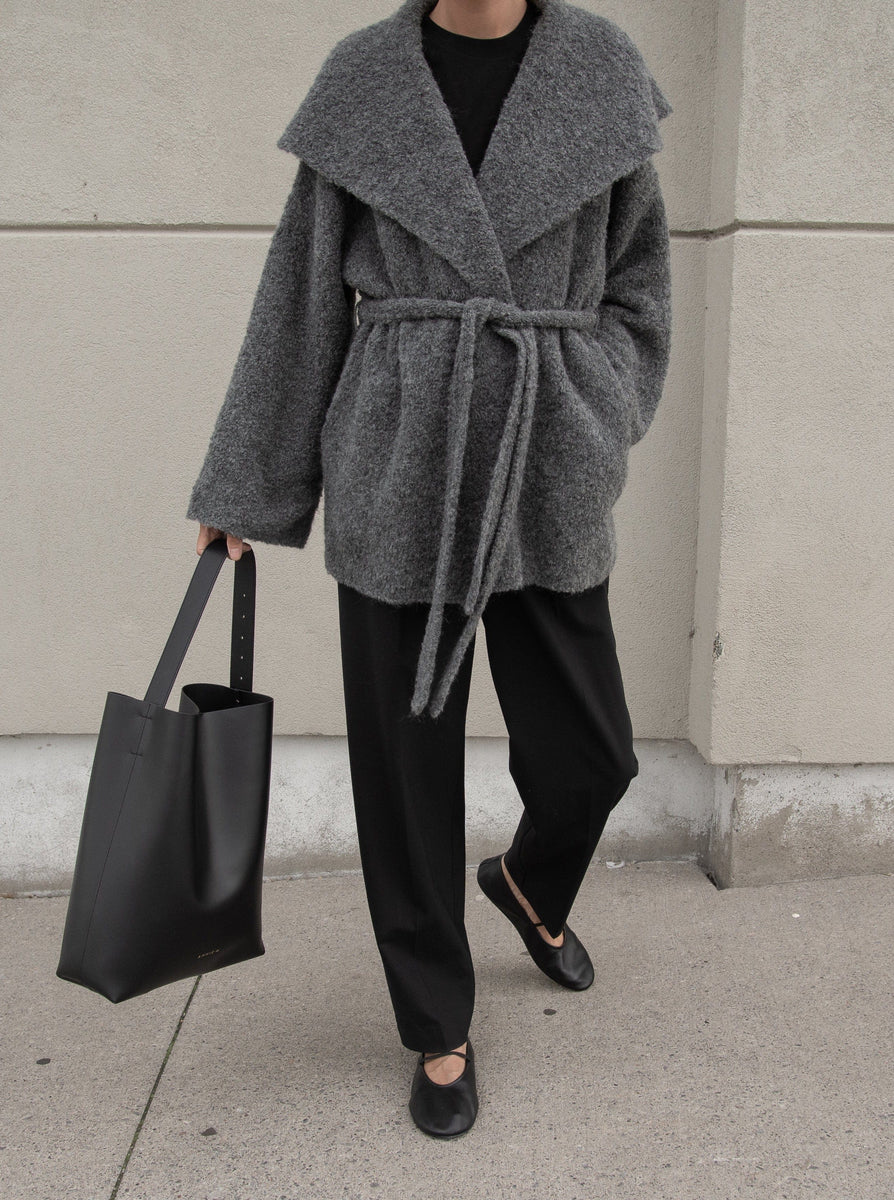 A woman wearing a cozy Canyon Wrap Sweater Coat - Charcoal Grey and black pants made of Alpaca fiber.