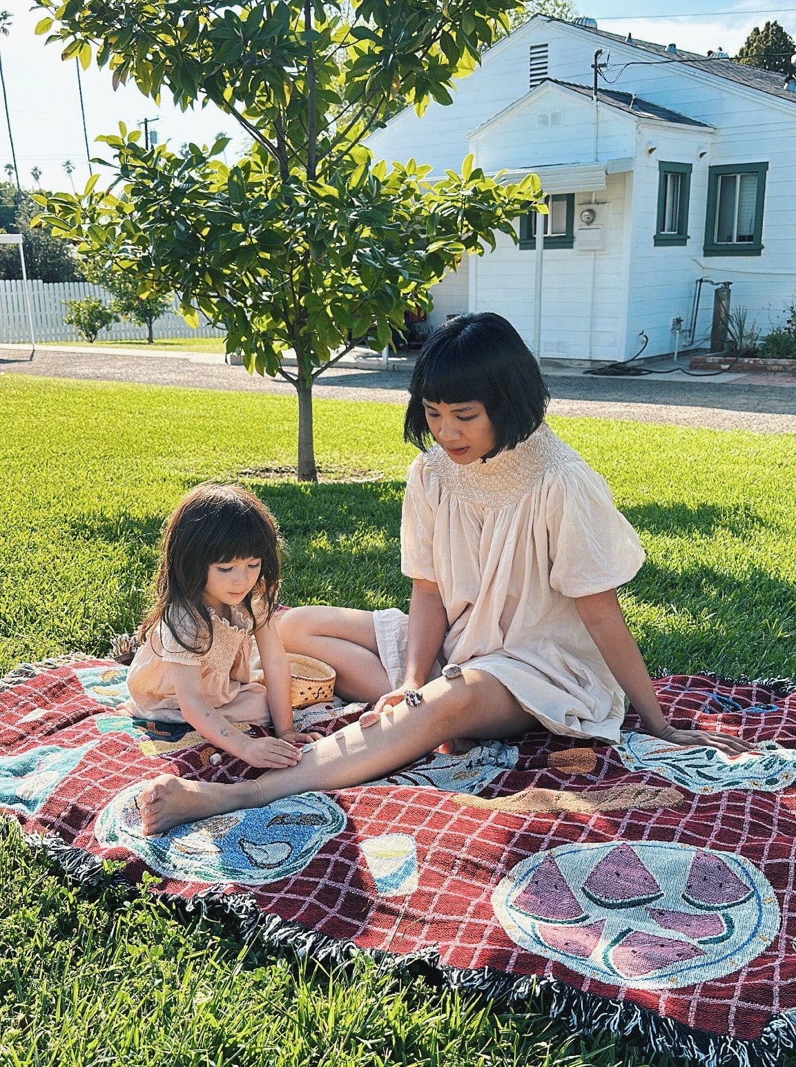 A woman and a child sitting on a Mirabel Mini Dress - Acacia Wood in the grass.