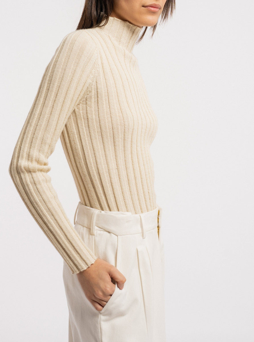The model is wearing a Soa Ribbed Turtleneck - Vanilla made of ethically-sourced baby alpaca.