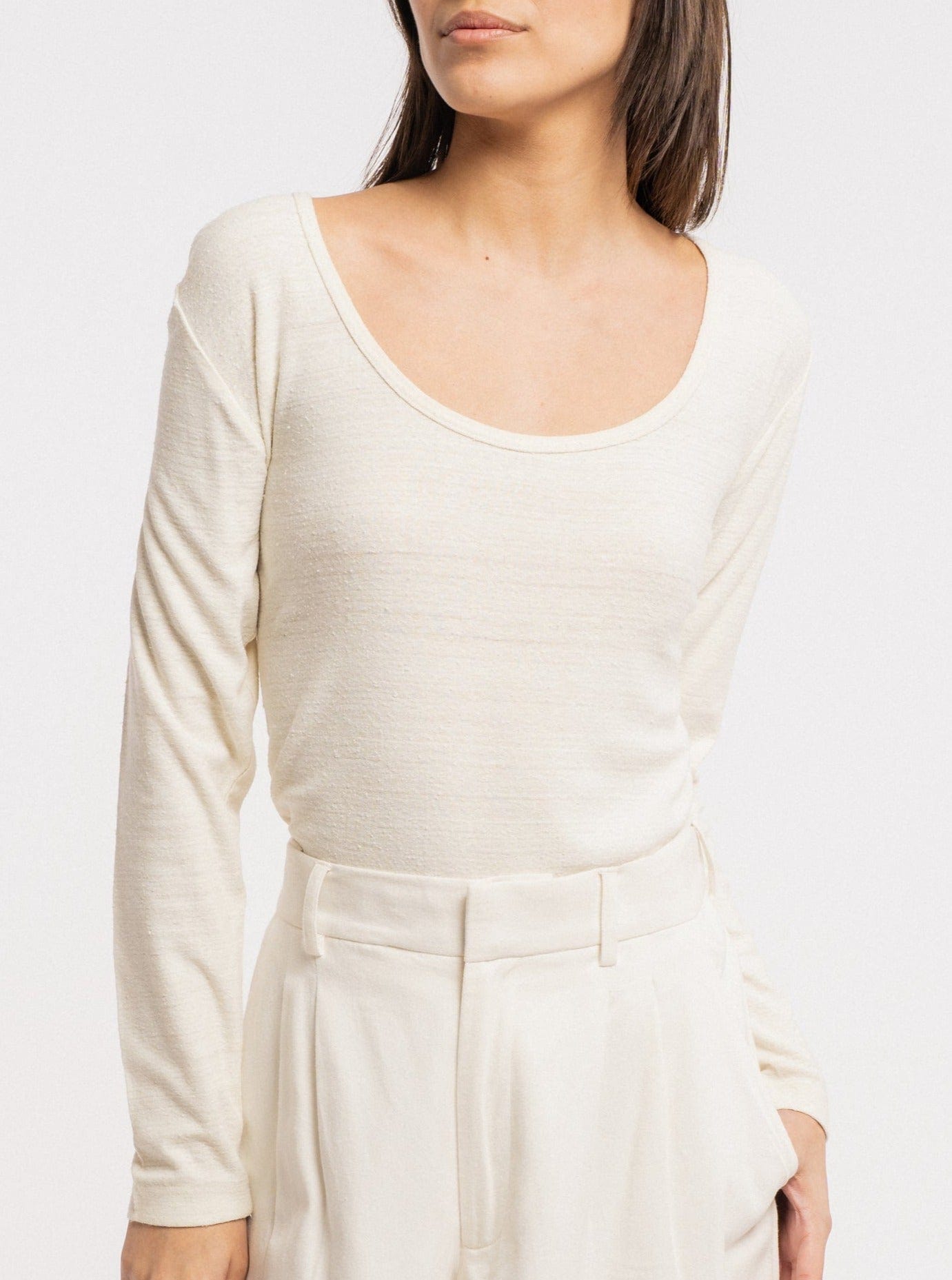 The model is wearing a white long-sleeved Scoop Neck Tee - Ivory made of silk noil, showcasing sustainability.