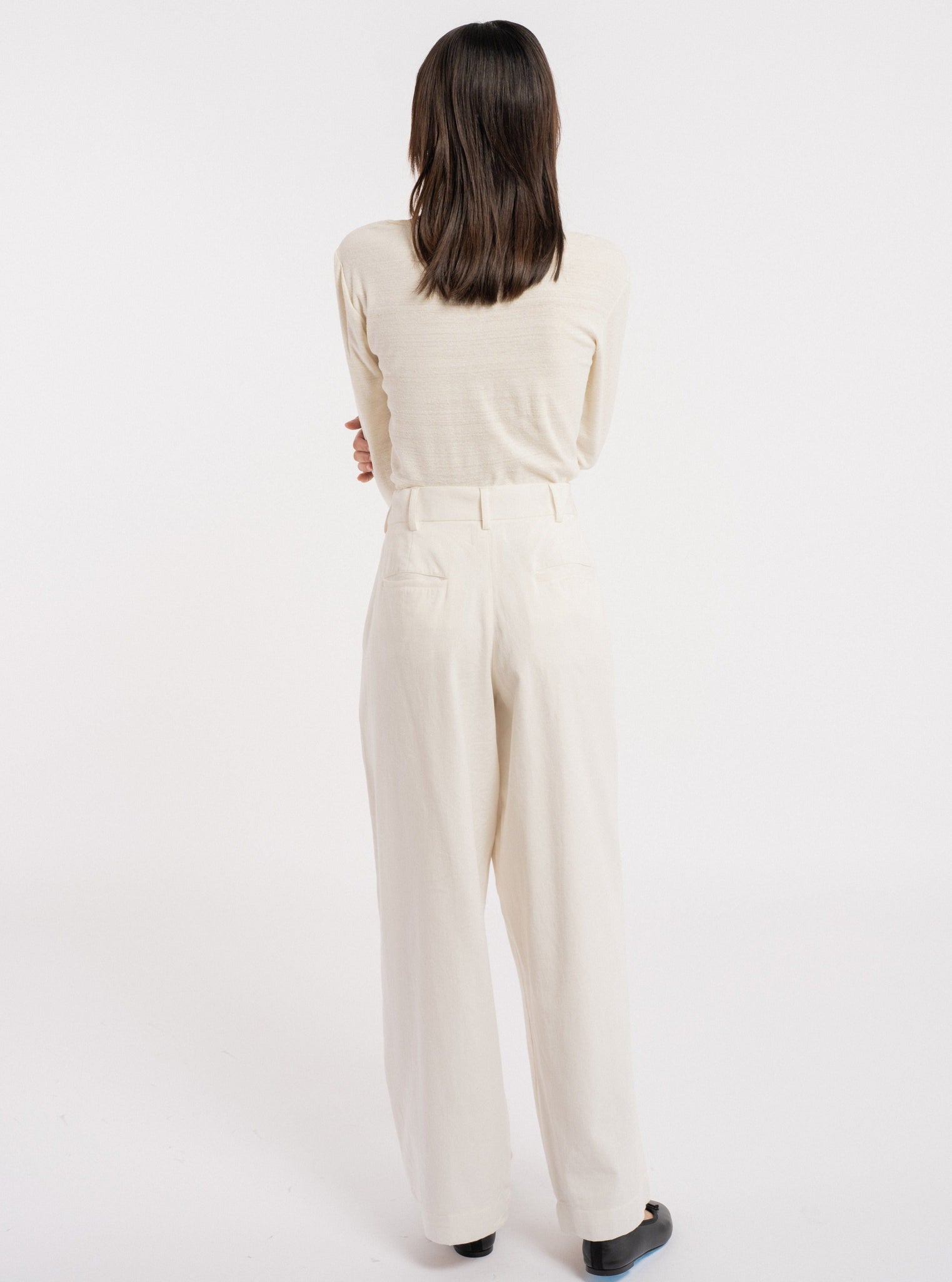 The back view of a woman wearing Ballet Scoop Tee - Ivory - pre-order wide leg pants.