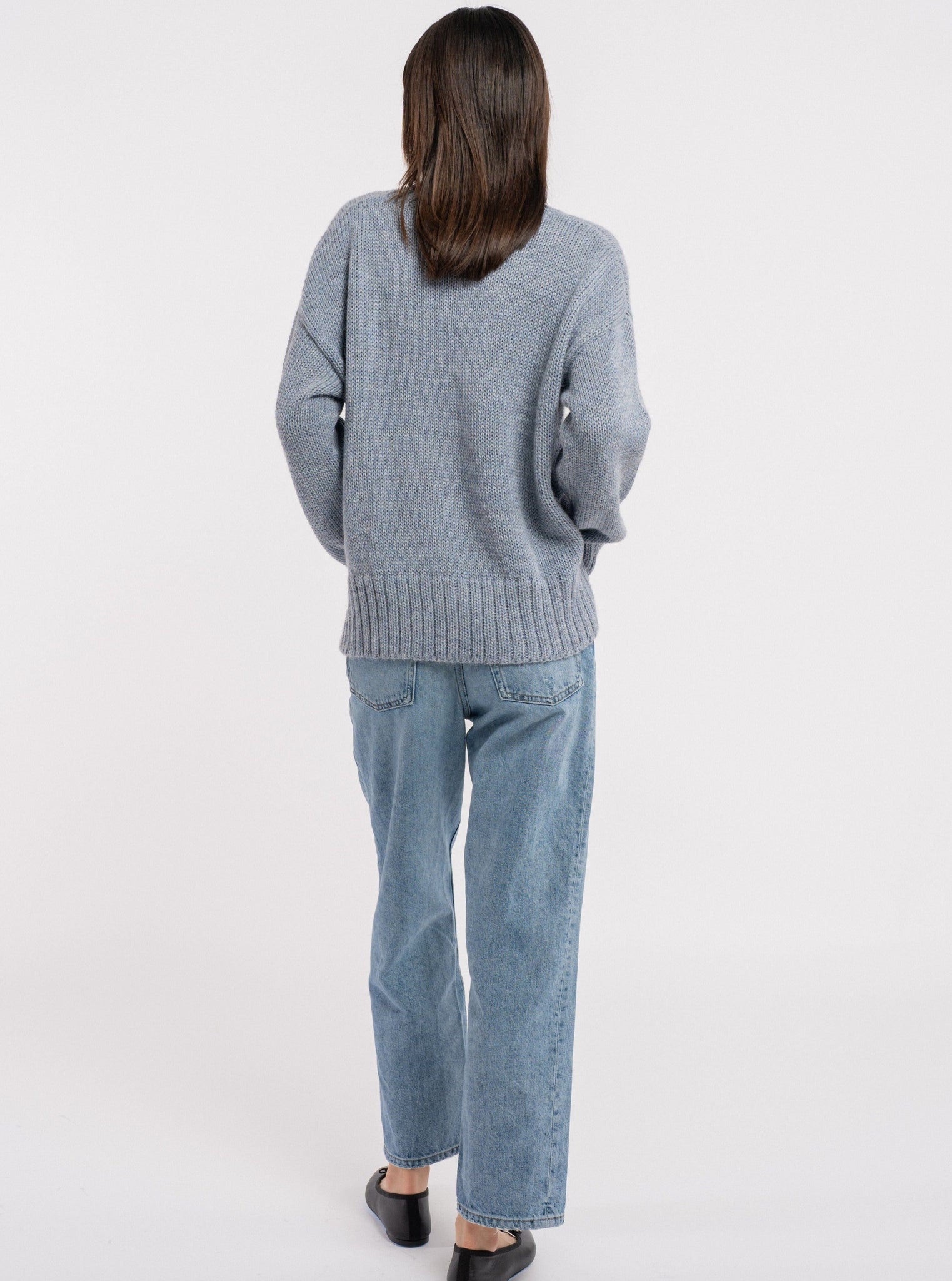 The back view of a woman wearing a cozy handmade Billy Sweater - Dusty Blue and jeans.