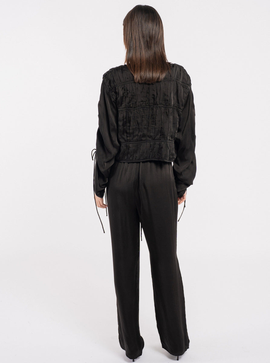 The Calla Top - Black, made from Bemberg cupro fabric and skillfully handmade in India, showcases the elegant back view of a woman in black attire.