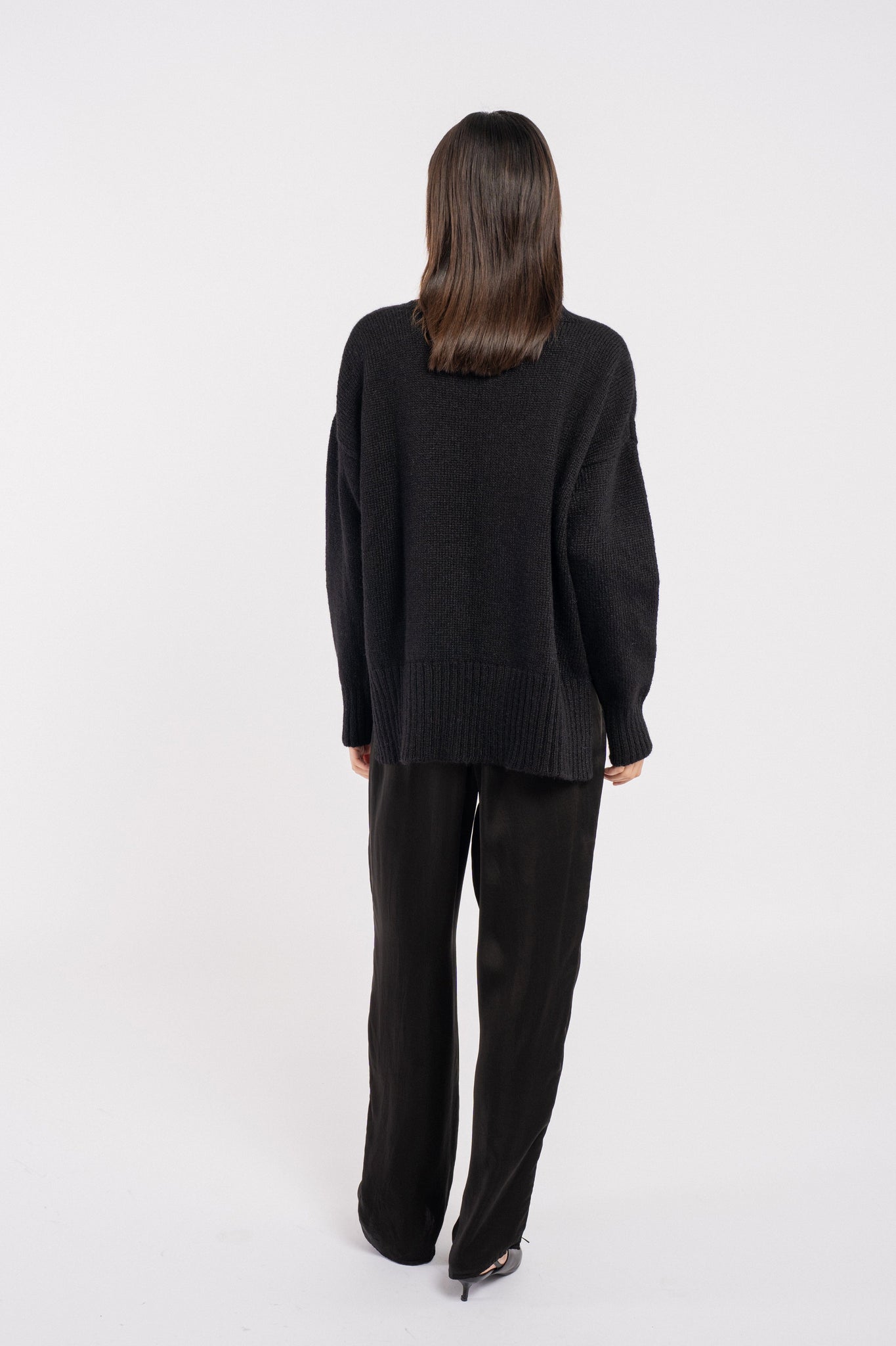 The back view of a woman wearing a Totto Sweater - Black - pre-order with ribbed trims.