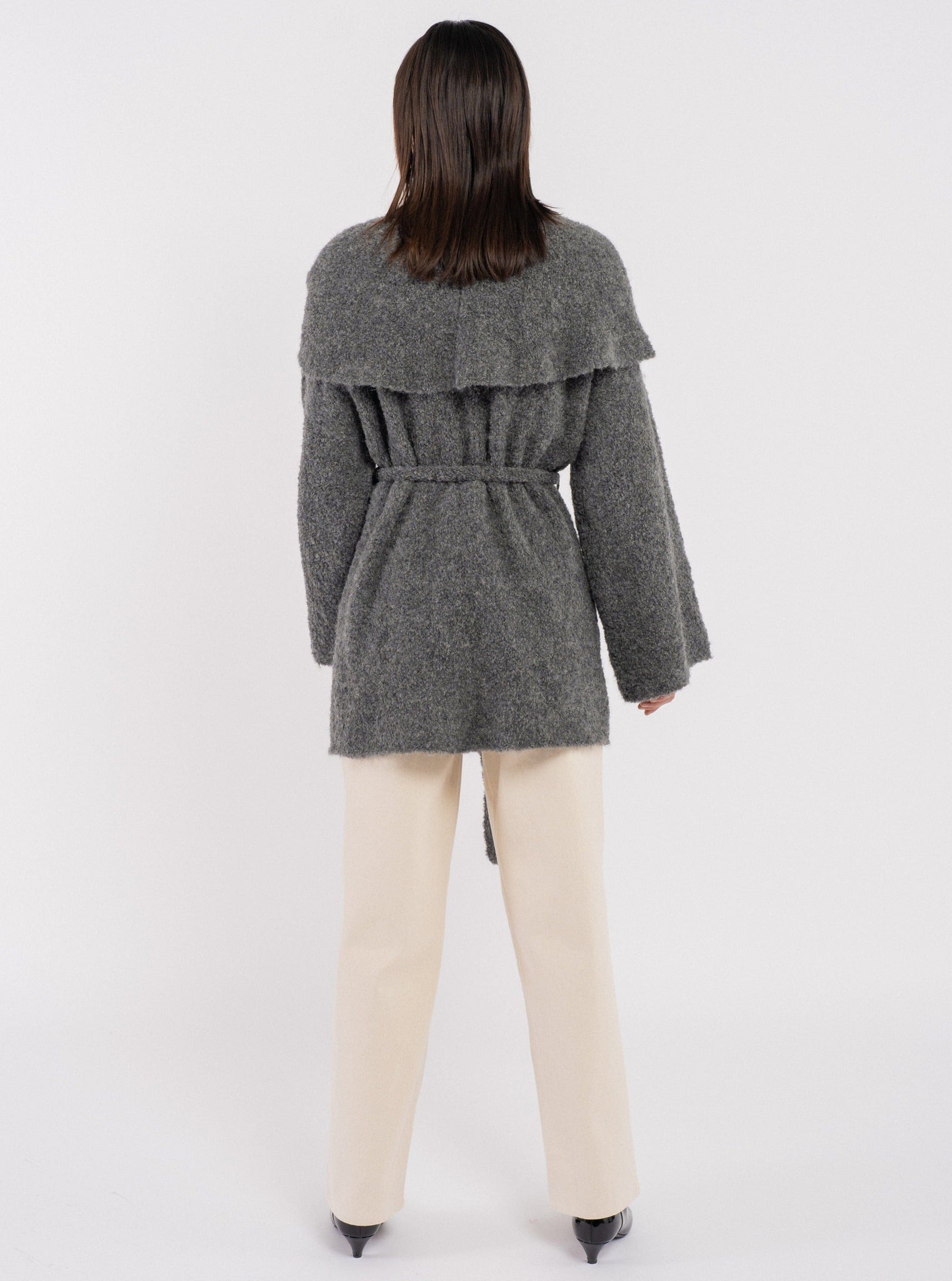 The back view of a woman wearing a Canyon Wrap Sweater Coat - Charcoal Grey and beige pants.