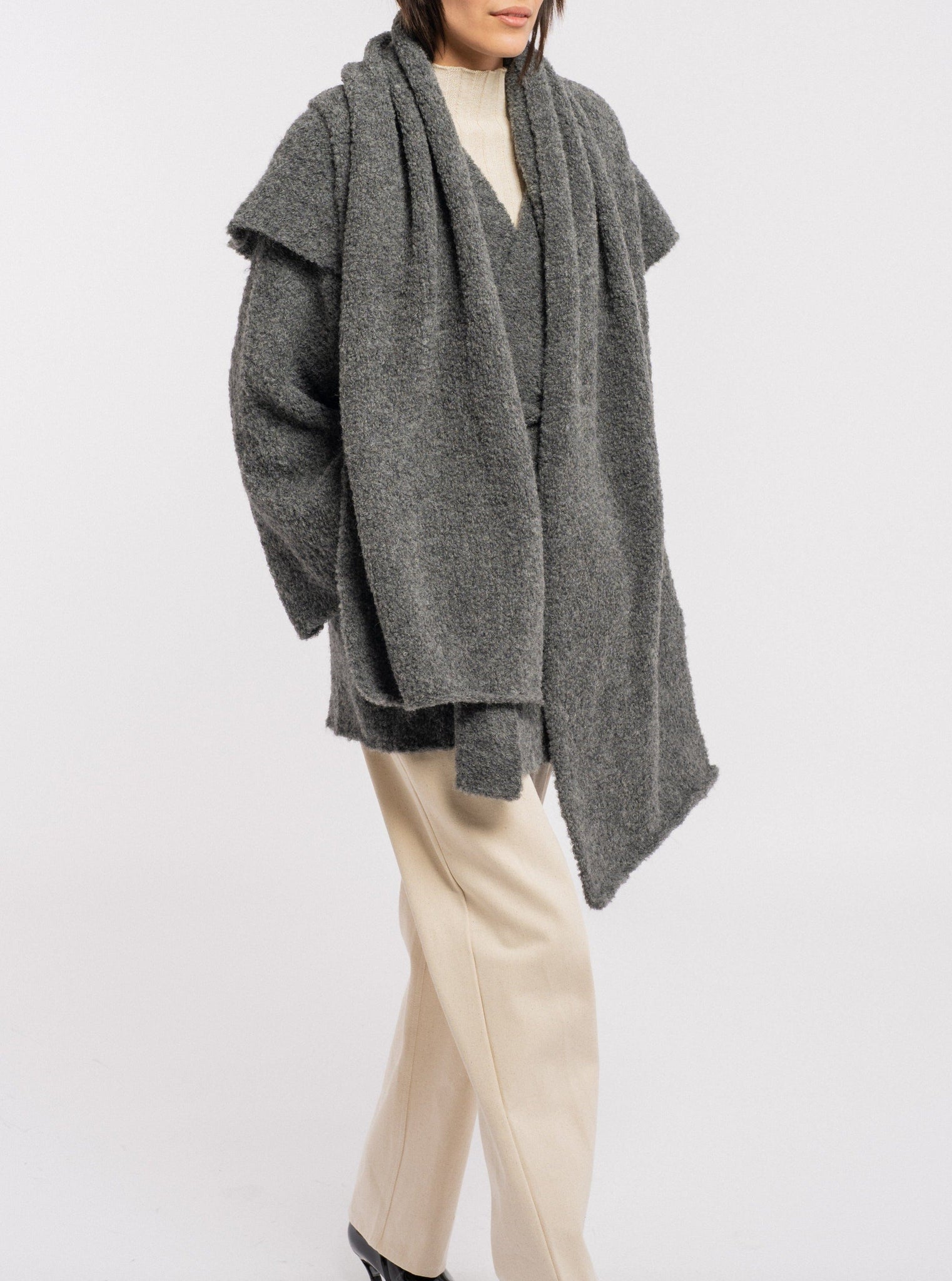 The model is wearing a Heirloom Knit Scarf - Charcoal Grey made with alpaca fiber and beige pants.