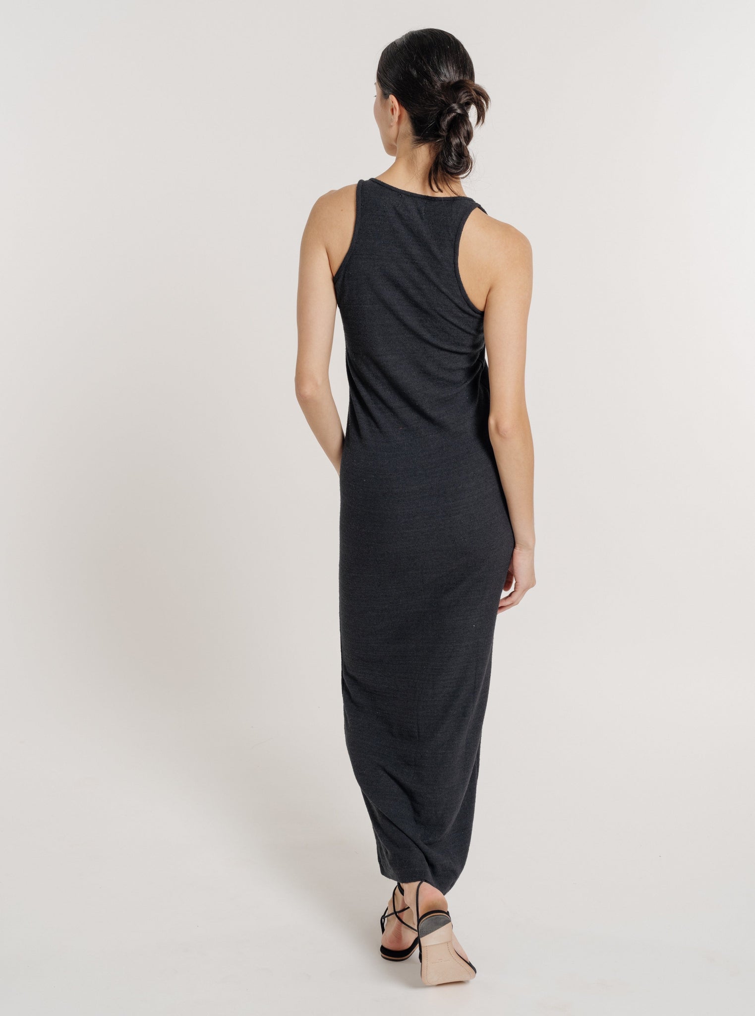 The back view of a woman wearing a Jersey Knit Tank Dress - Black Silk Noil - Pre-order made of textured fabric.