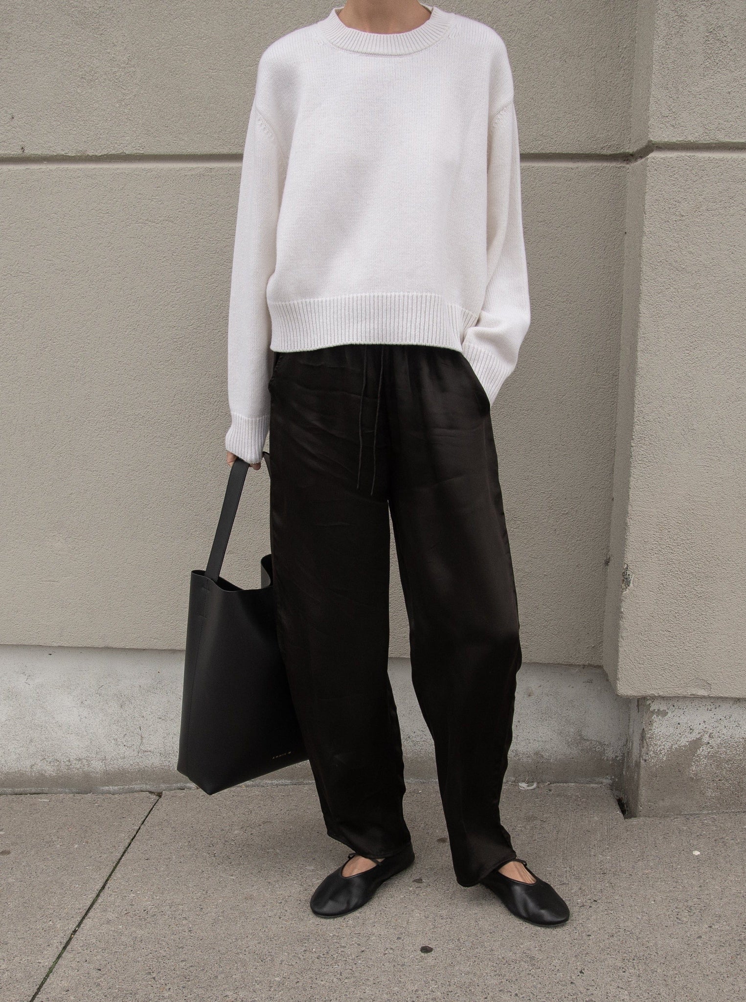 A woman wearing a sustainable Bemberg Cupro white sweater and the Leonie Pant - Black.