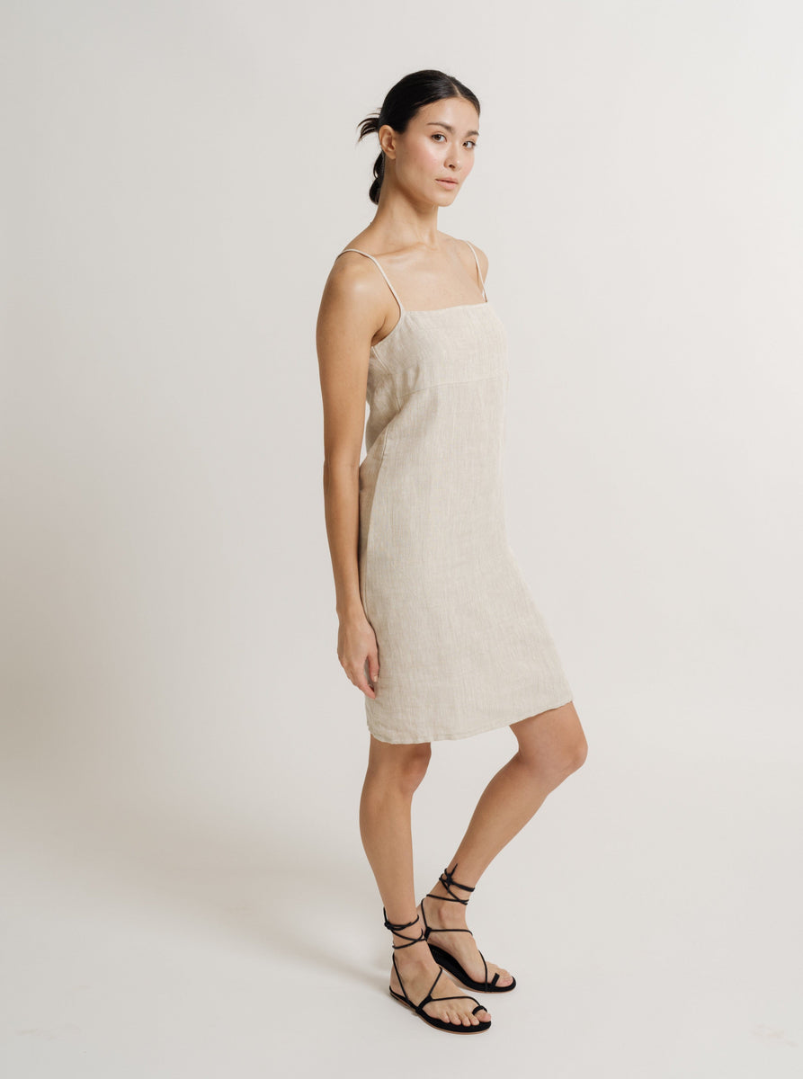 A model wearing the Linen Mini Dress - Natural Linen - Pre-order with adjustable straps and sandals.