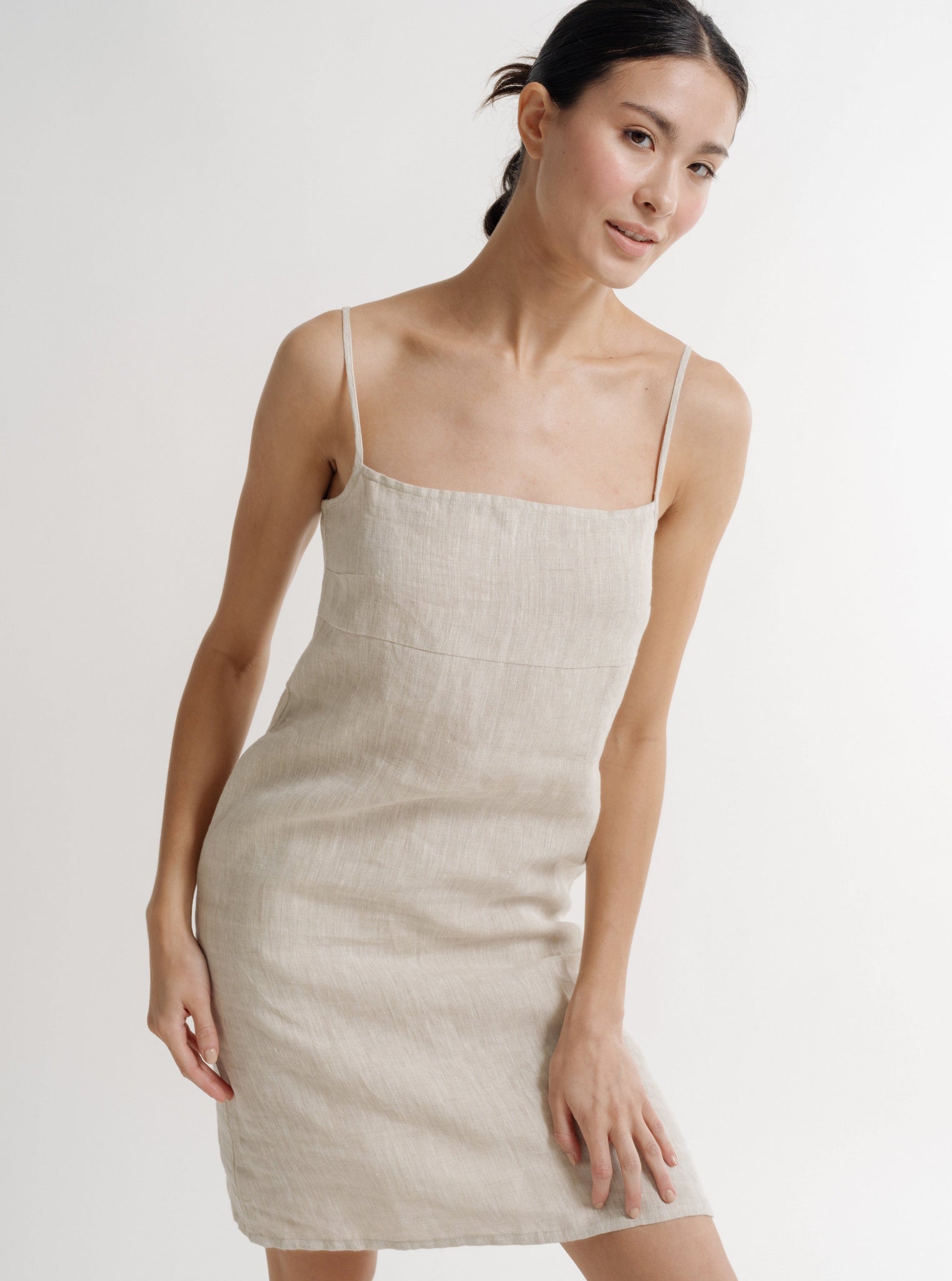 The model is wearing a Linen Mini Dress - Natural Linen - Pre-order with adjustable straps and a square neckline.