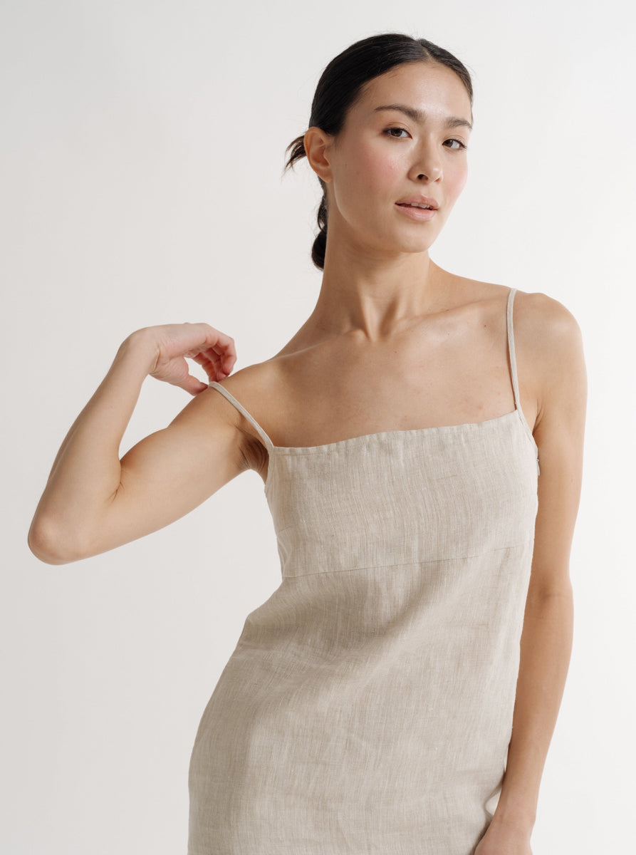 The model is wearing a Natural Linen Mini Dress with adjustable straps and a square neckline.