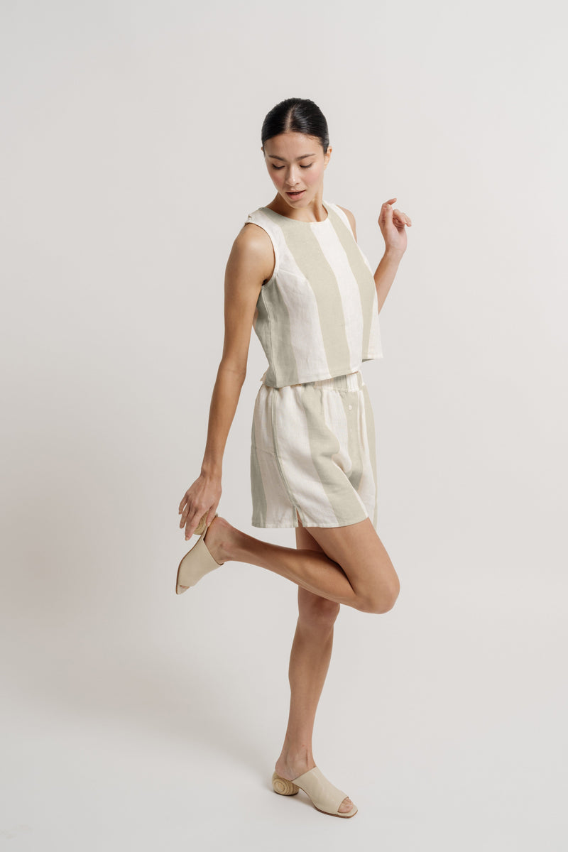 A model wearing an Open Back Tank - Tulum Stripe romper and sandals made from organic linen.