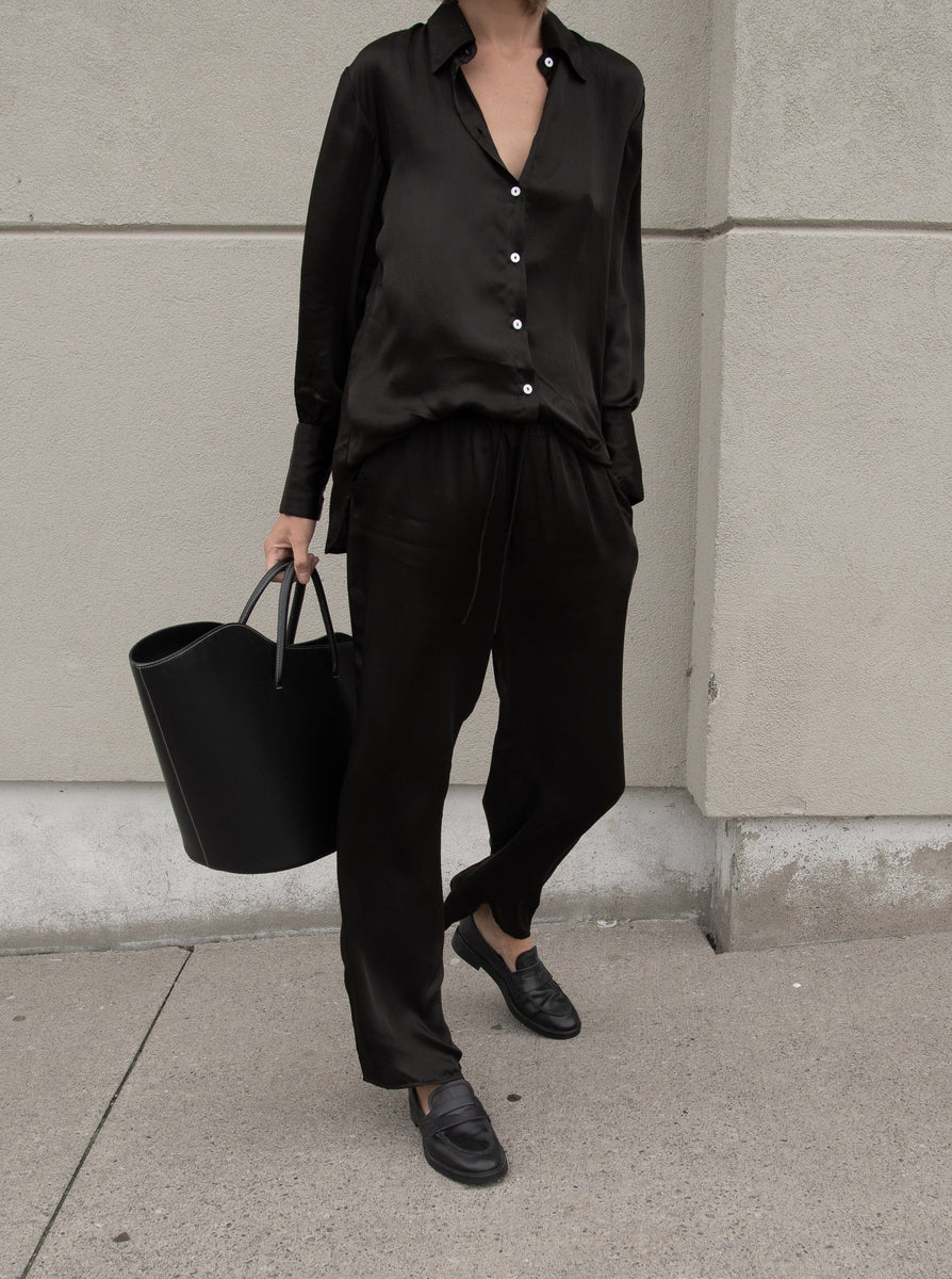 A woman wearing black pants and the Museo Button Up - Black Cupro with a slimmer cut.