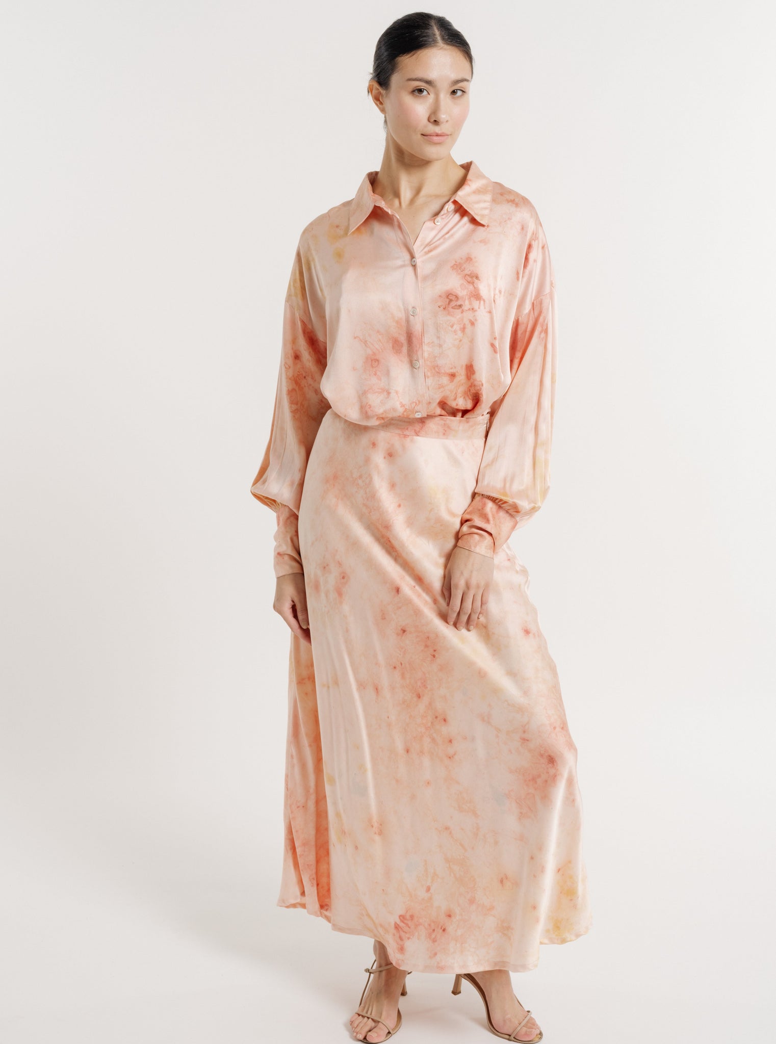 Woman posing in a Museo Silk Button Up - Botanical Ice Dye, peach-toned watercolor dress.