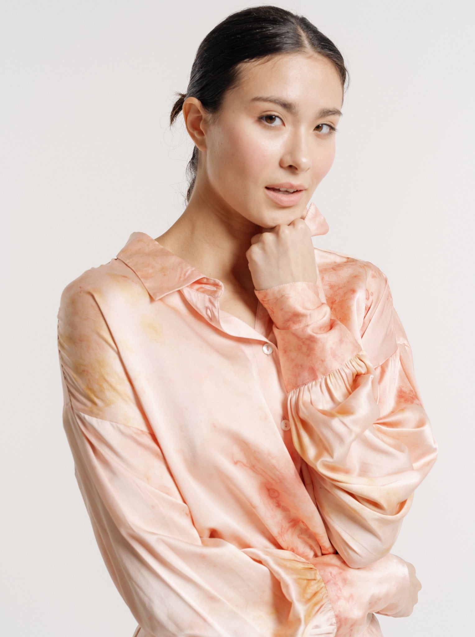 A woman in a 100% silk, Museo Silk Button Up - Botanical Ice Dye blouse is posing with her hand on her chin.
