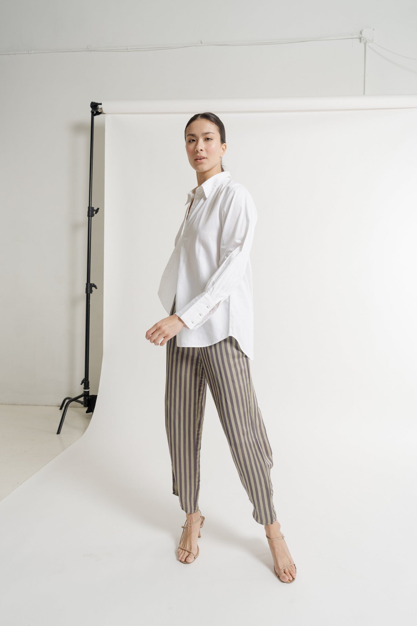 A model wearing a white shirt and the Ruffled Waist Tie Pant - Urban Stripe - Pre-order. These pants, known as the Cropped Ruffled Waist Tie Pant, are currently available for resort pre-orders.