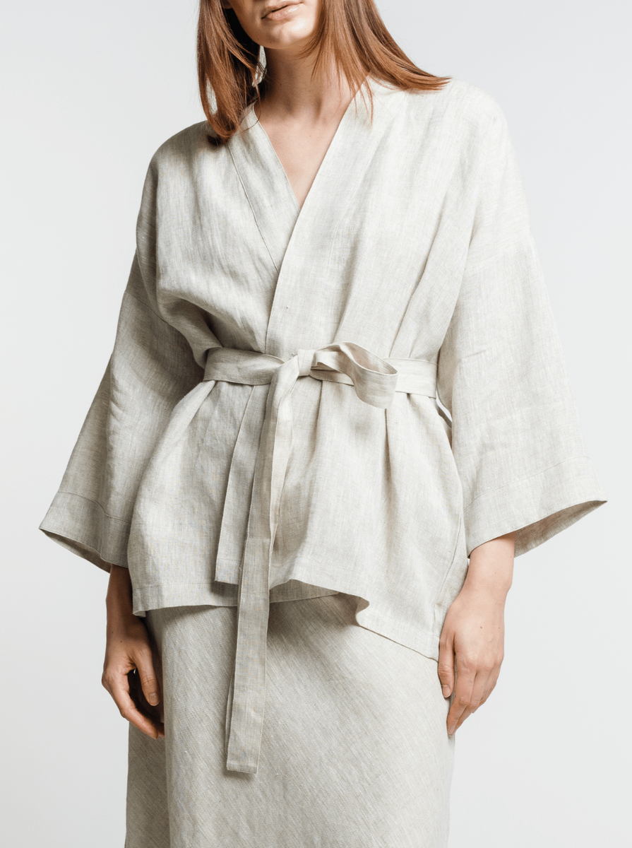 Woman modeling a light-colored organic Linen Wrap Top - Natural with a tie waist and flared sleeves, paired with black strappy sandals.