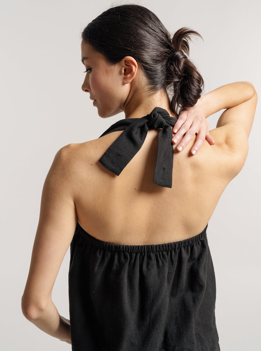The back of a woman wearing a Cross Back Tank - Black Silk Noil - Pre-order, adorned with a bow.