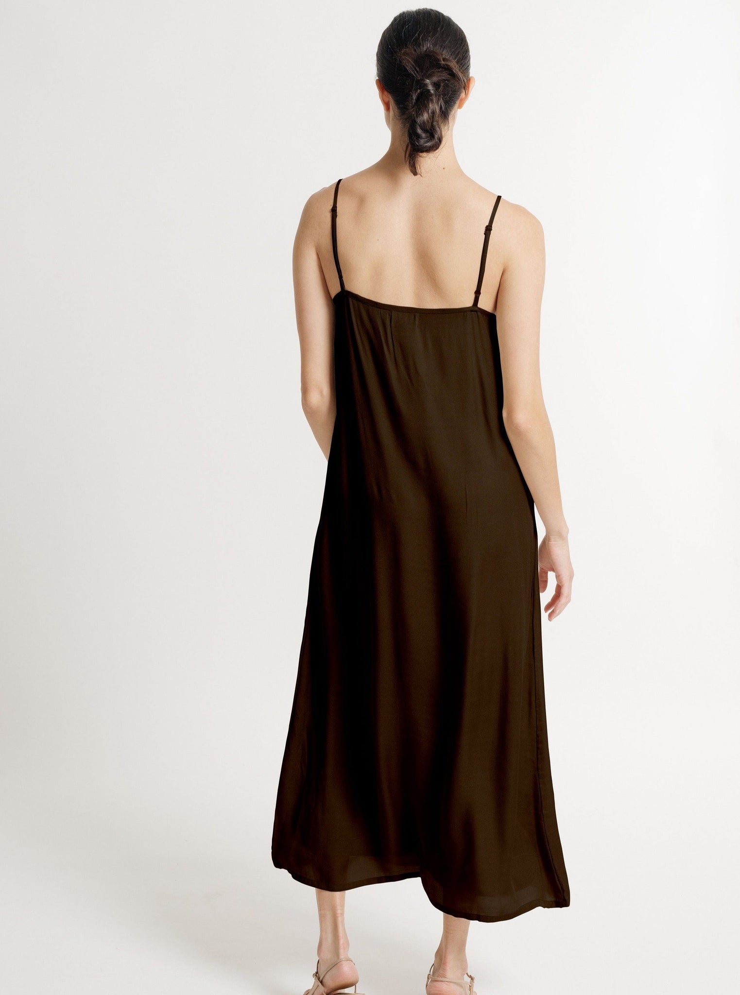 The back view of a woman wearing the Kate Dress - Basalt Brown, a sustainably made brown slip dress handmade in India.