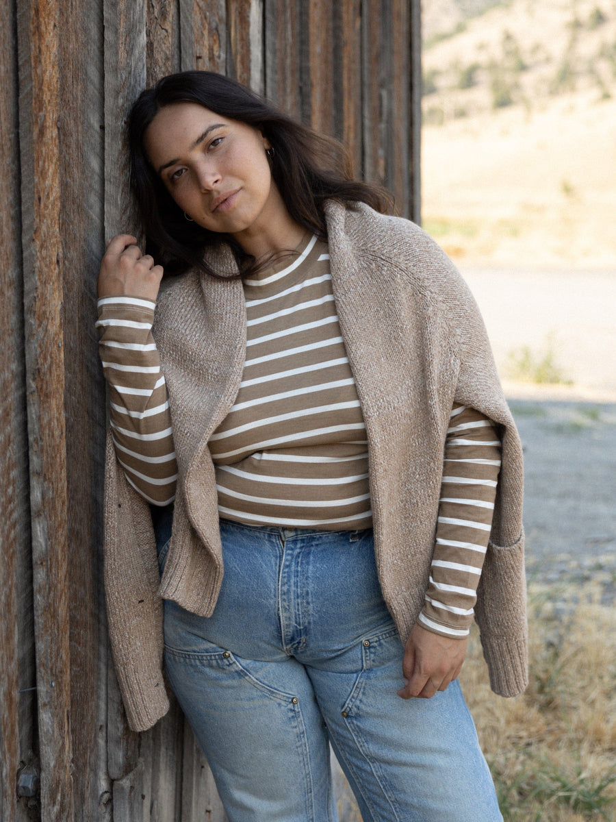 A fit woman in jeans and a Sample 144 - Mock Neck Long Sleeve Tee - Tannin Stripe leaning against a barn.