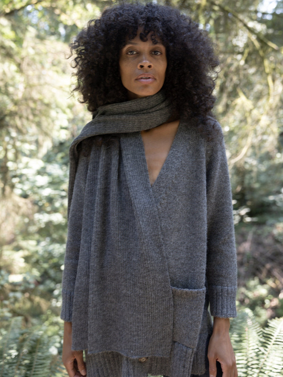 A woman wearing a grey sweater and Alpaca Ribbed Scarf - Smoke in the woods.
