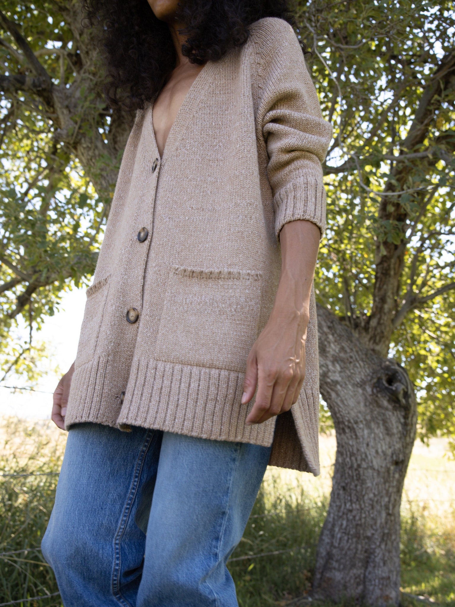 A woman wearing jeans and a Valley Cardigan - Caramel.