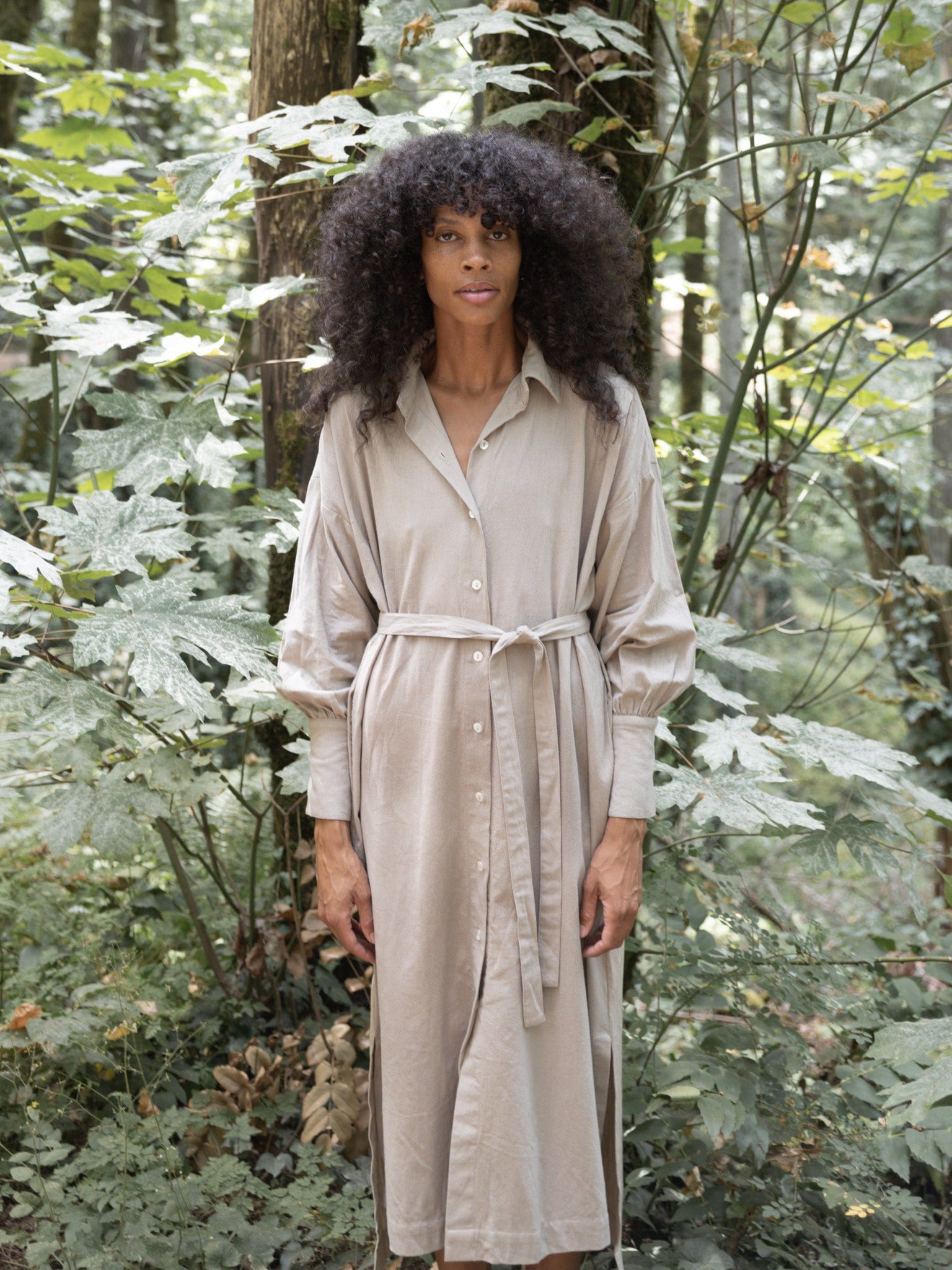A woman in a Dillon Dress - Mushroom - XXL - Sample, made of organic cotton, standing in the woods.