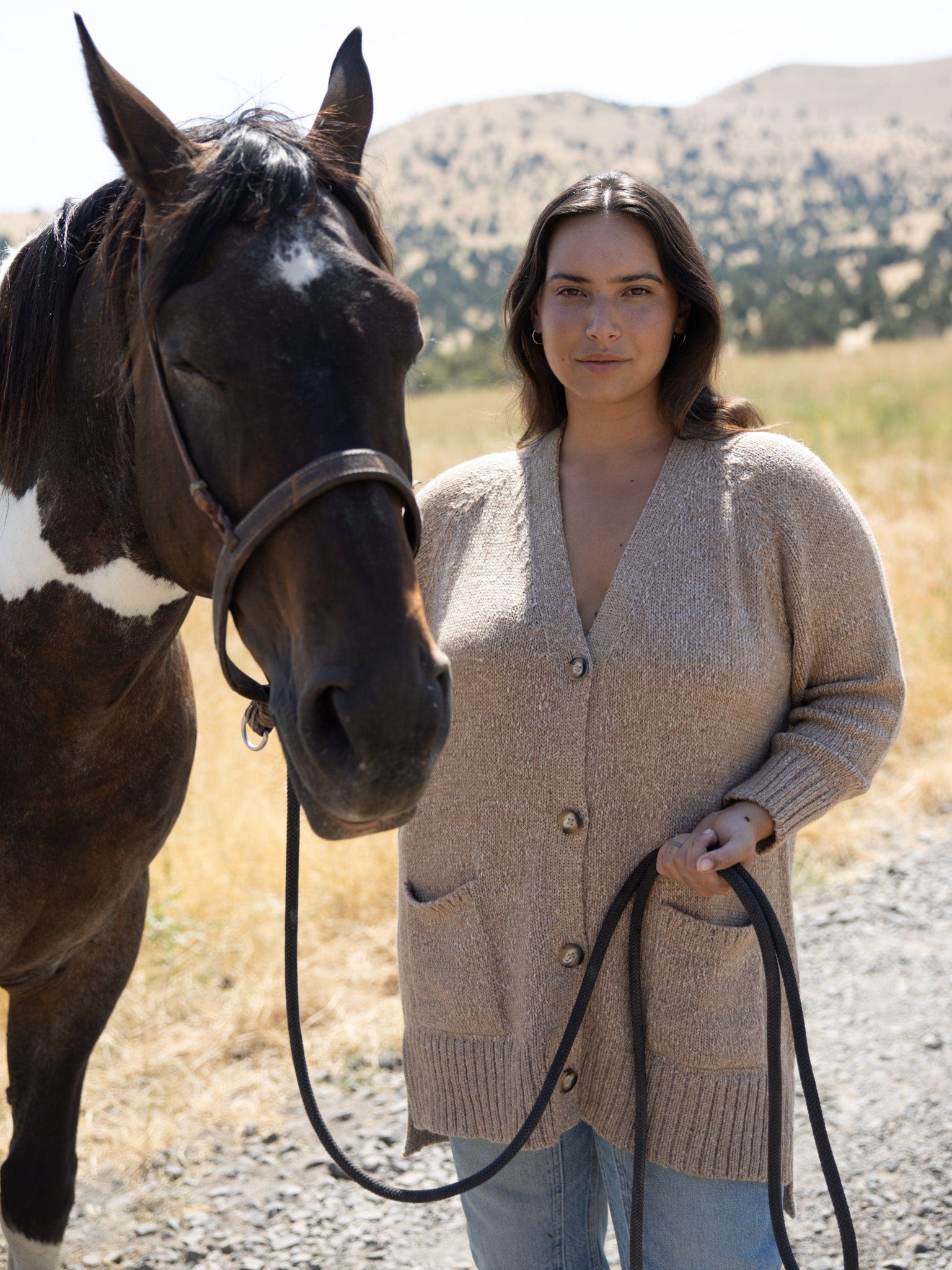 A woman standing next to a Valley Cardigan - Caramel.