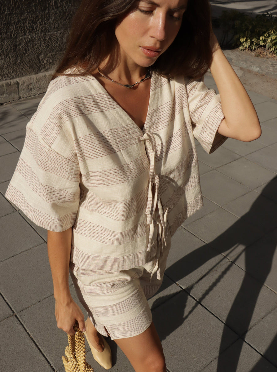 A woman in an Everyday Short - Terracotta Ticking Stripe and striped top made from organic cotton walking down a sidewalk.
