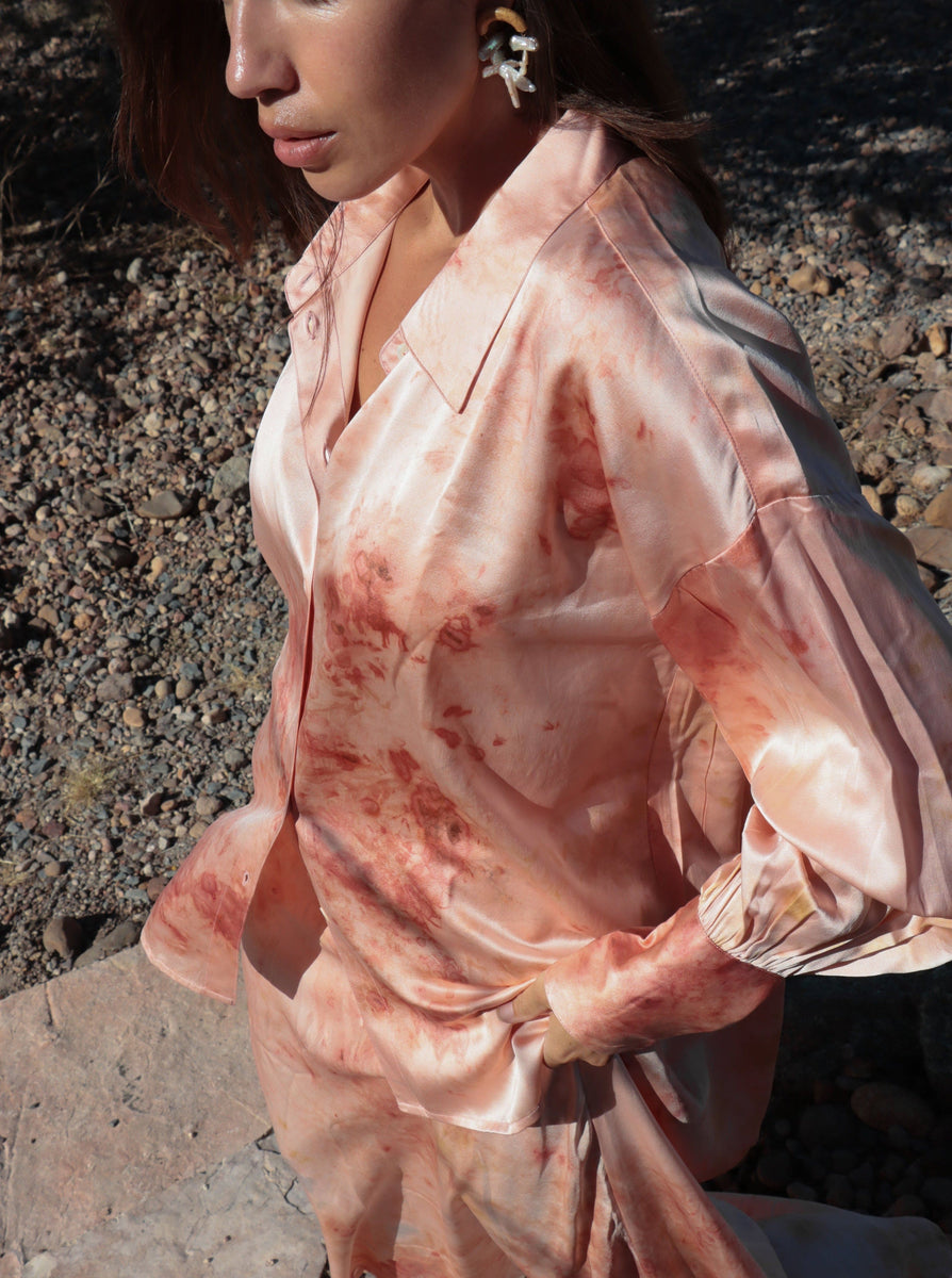 A person outdoors wearing a 100% silk Museo Silk Button Up - Botanical Ice Dye with a gradient of red and cream, standing in a rocky terrain.