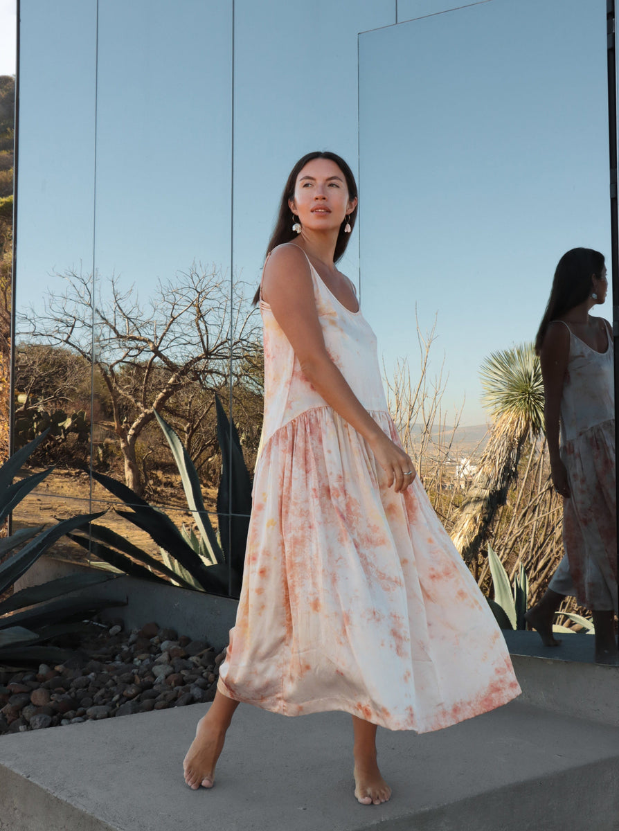 Woman in a Silk Midi Slip Dress - Botanical Ice Dye standing barefoot by a mirror in a desert setting.