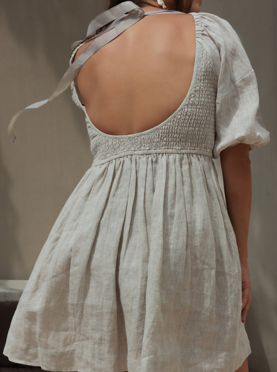 A woman wearing the Carmen Mini Dress - Natural with an open back and ribbon tie detail.