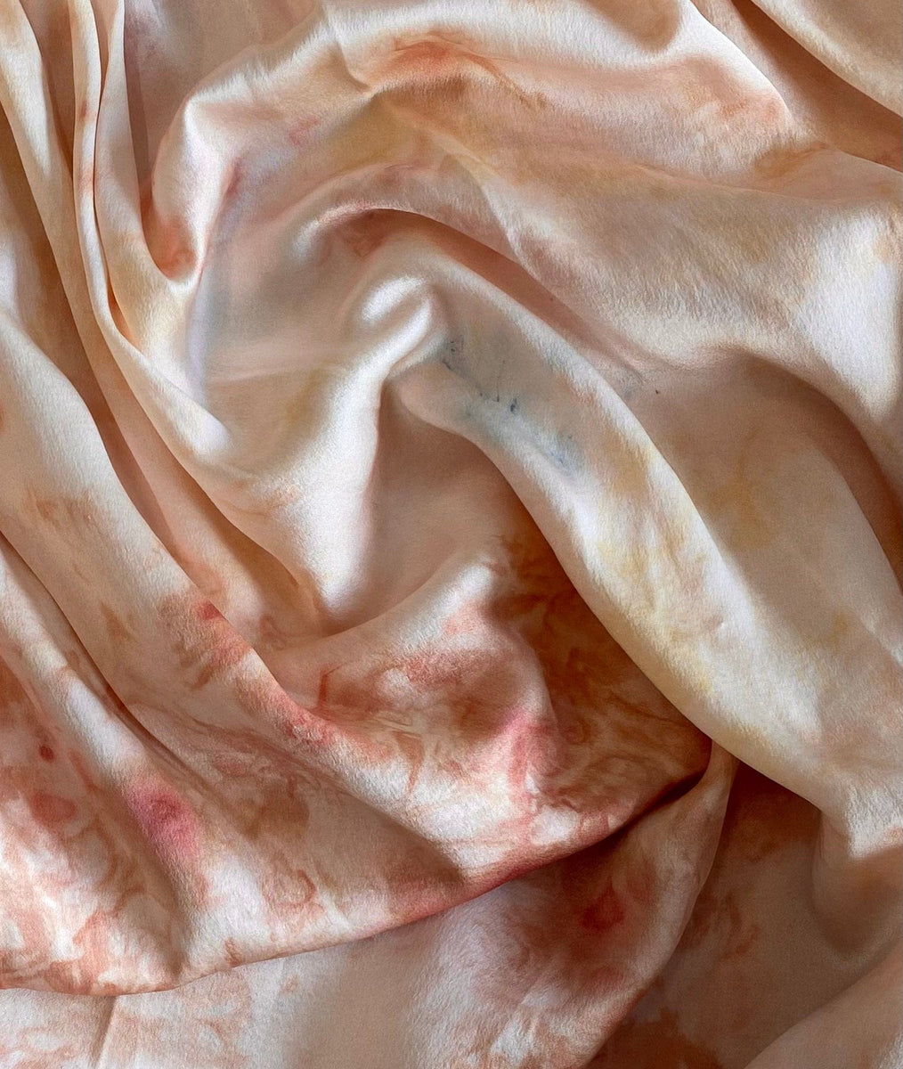 Close-up of a wrinkled peach-colored Museo Silk Button Up - Botanical Ice Dye fabric with subtle discolorations.