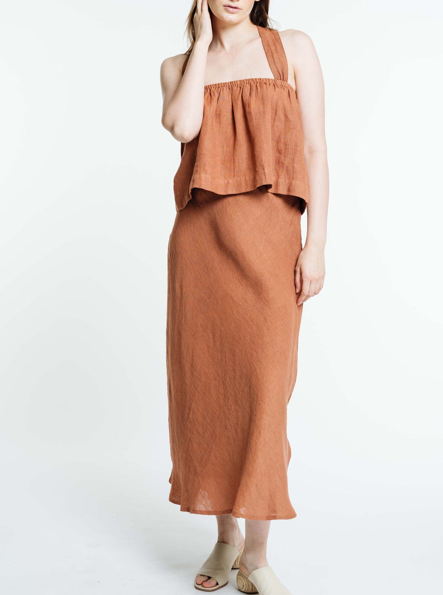 The model is wearing a handmade Jardín Midi Skirt in Amber Brown made from organic linen.