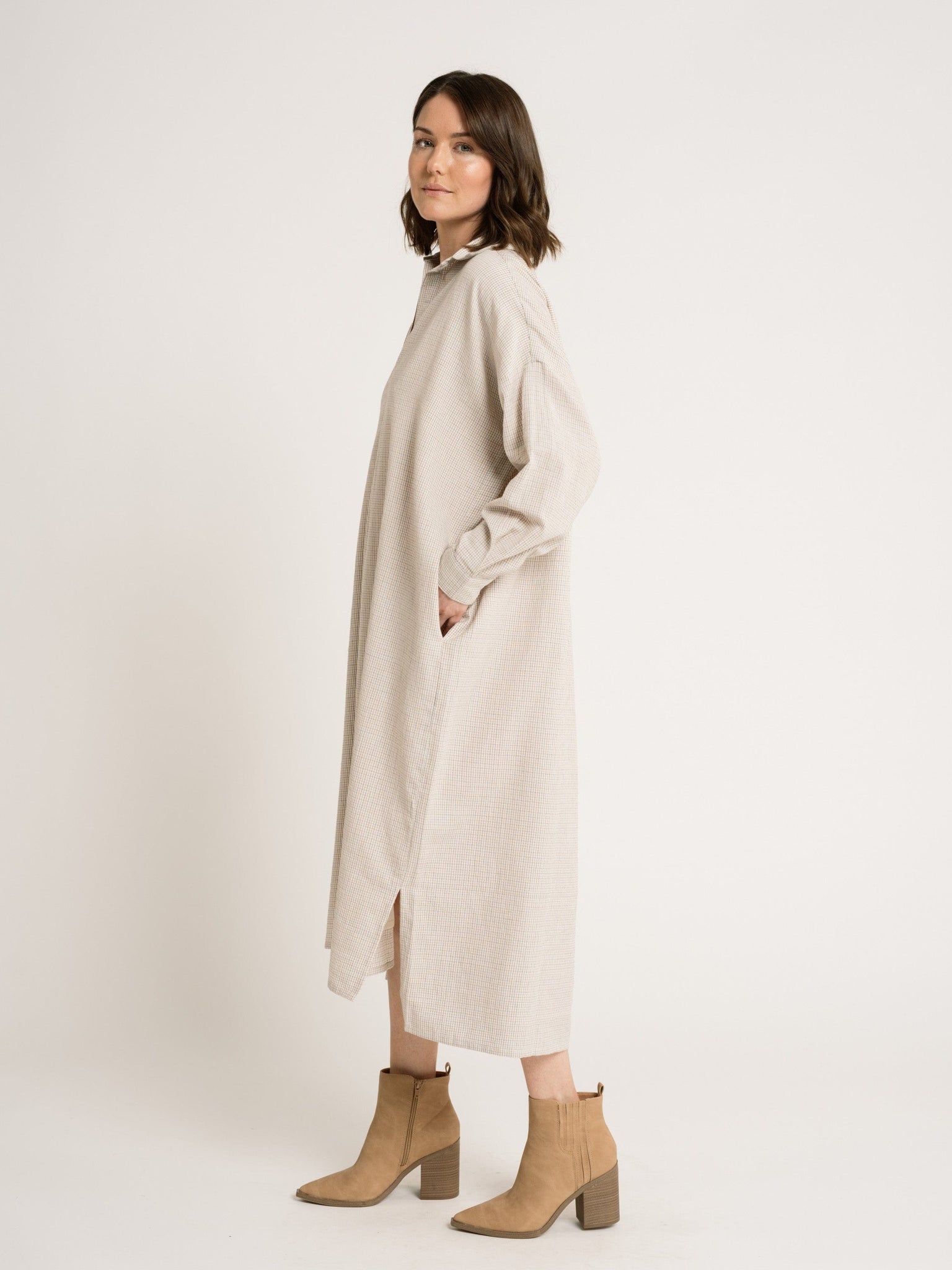 The model is wearing an Oversized Tunic Dress - Dove Small Grid made of organic cotton with tan boots.