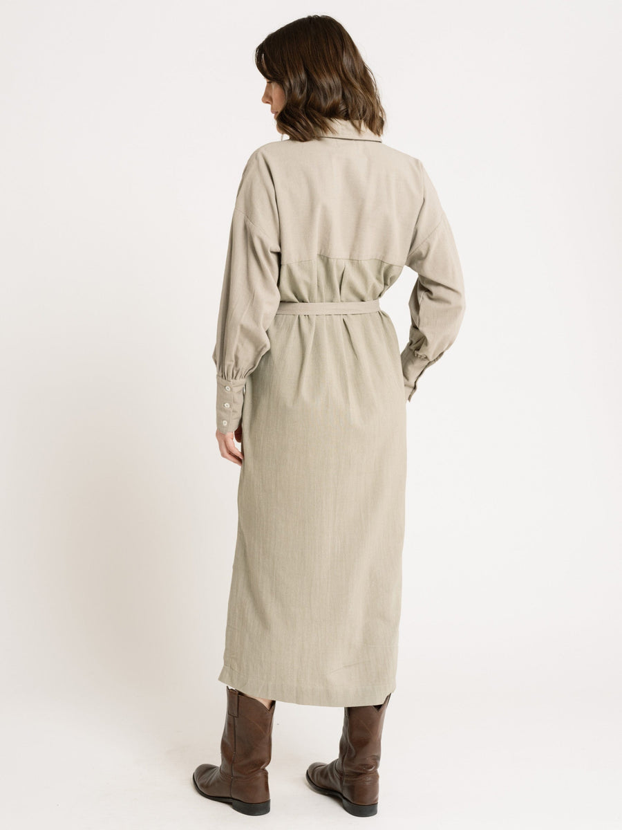 The back view of a woman wearing a Dillon Dress - Mushroom - XXL - Sample made of organic cotton and cowboy boots.