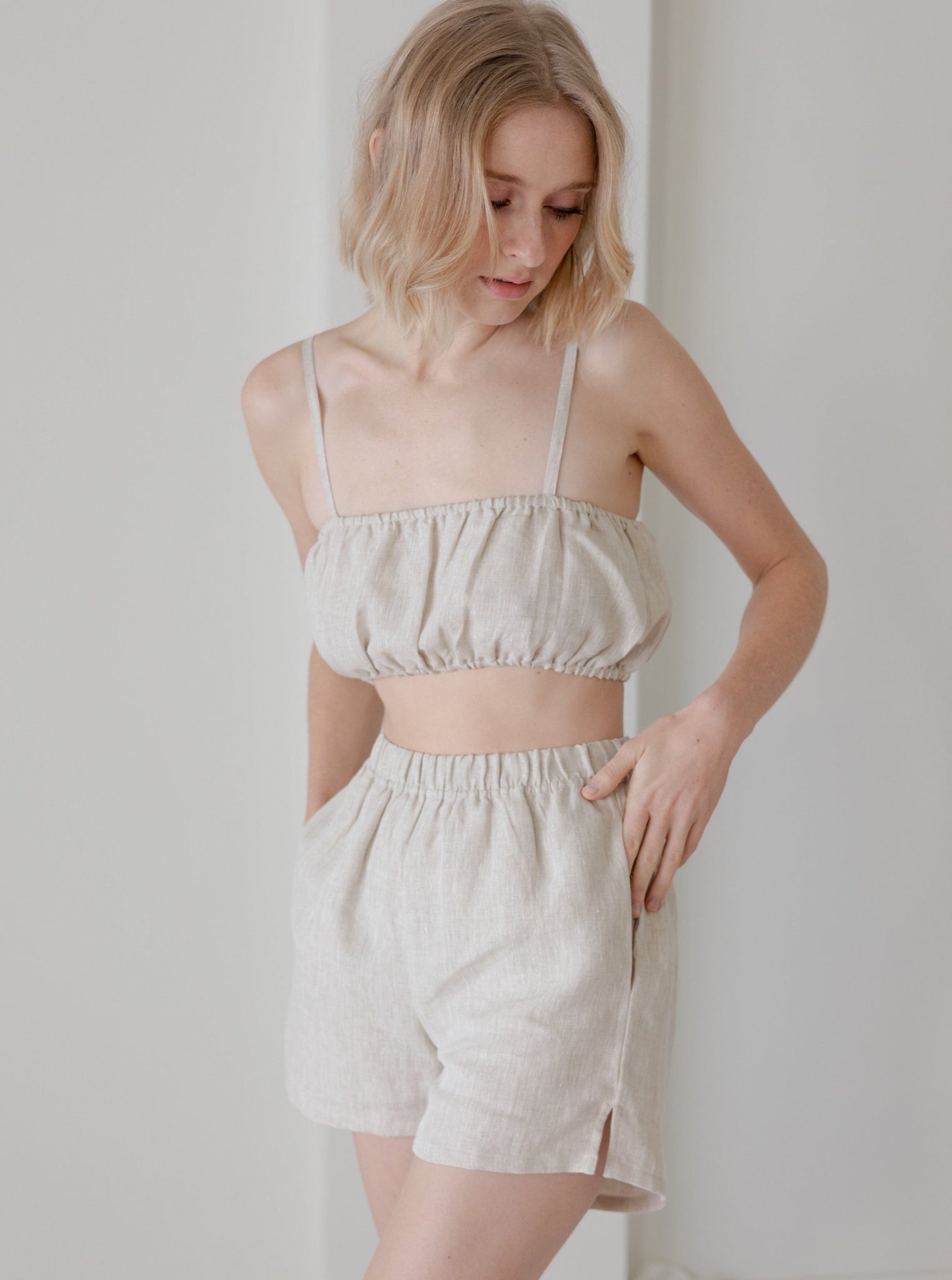 The model is wearing a white organic linen Elastic Bandeau - Natural - Sample and shorts.