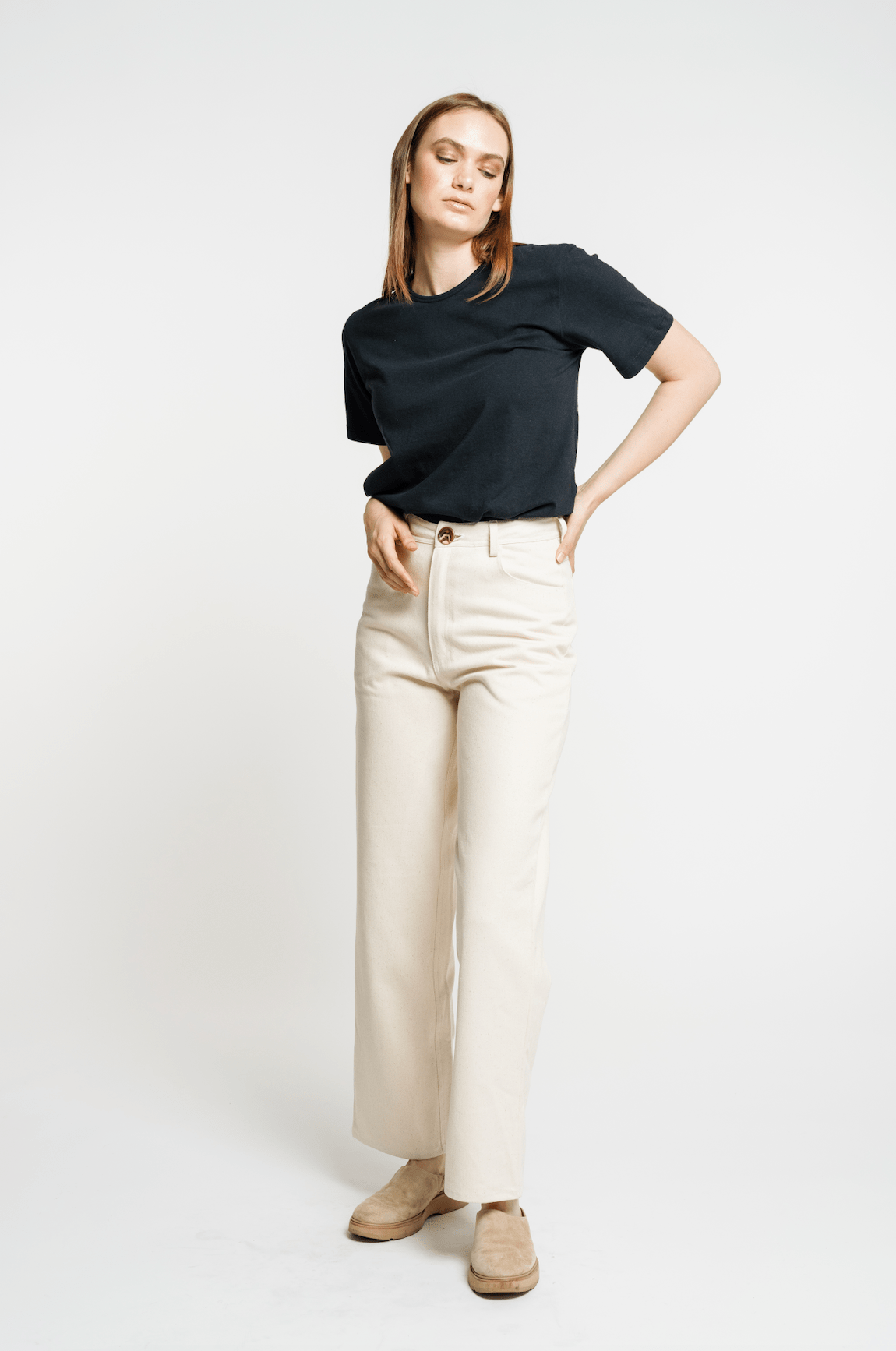 The model is wearing a sustainable black Crewneck T-Shirt and beige wide leg pants made from organic cotton.