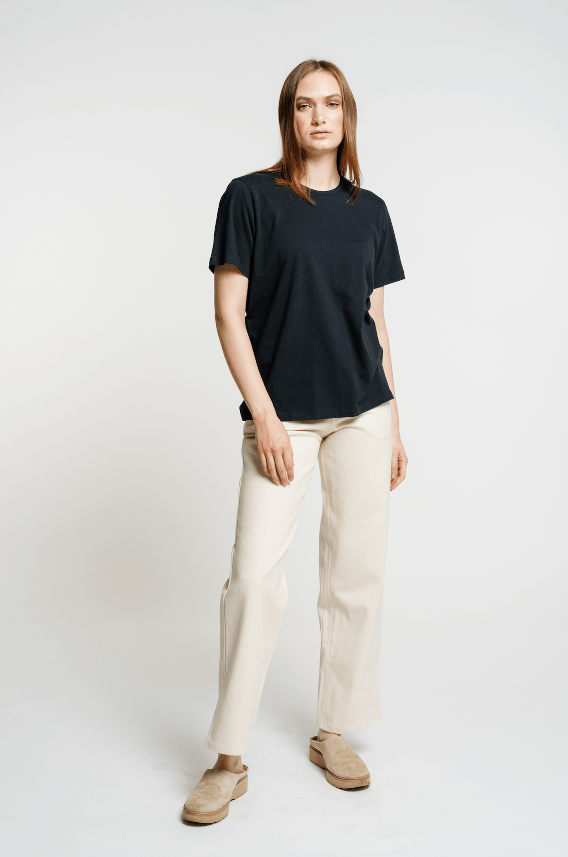 The model is wearing a sustainable Crewneck T-Shirt in black and organic cotton pants in beige.