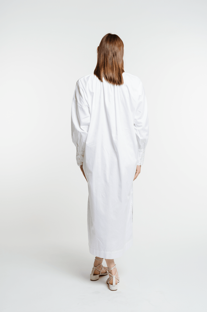 The back view of a woman wearing a Dolores Dress - White made of crisp cotton.