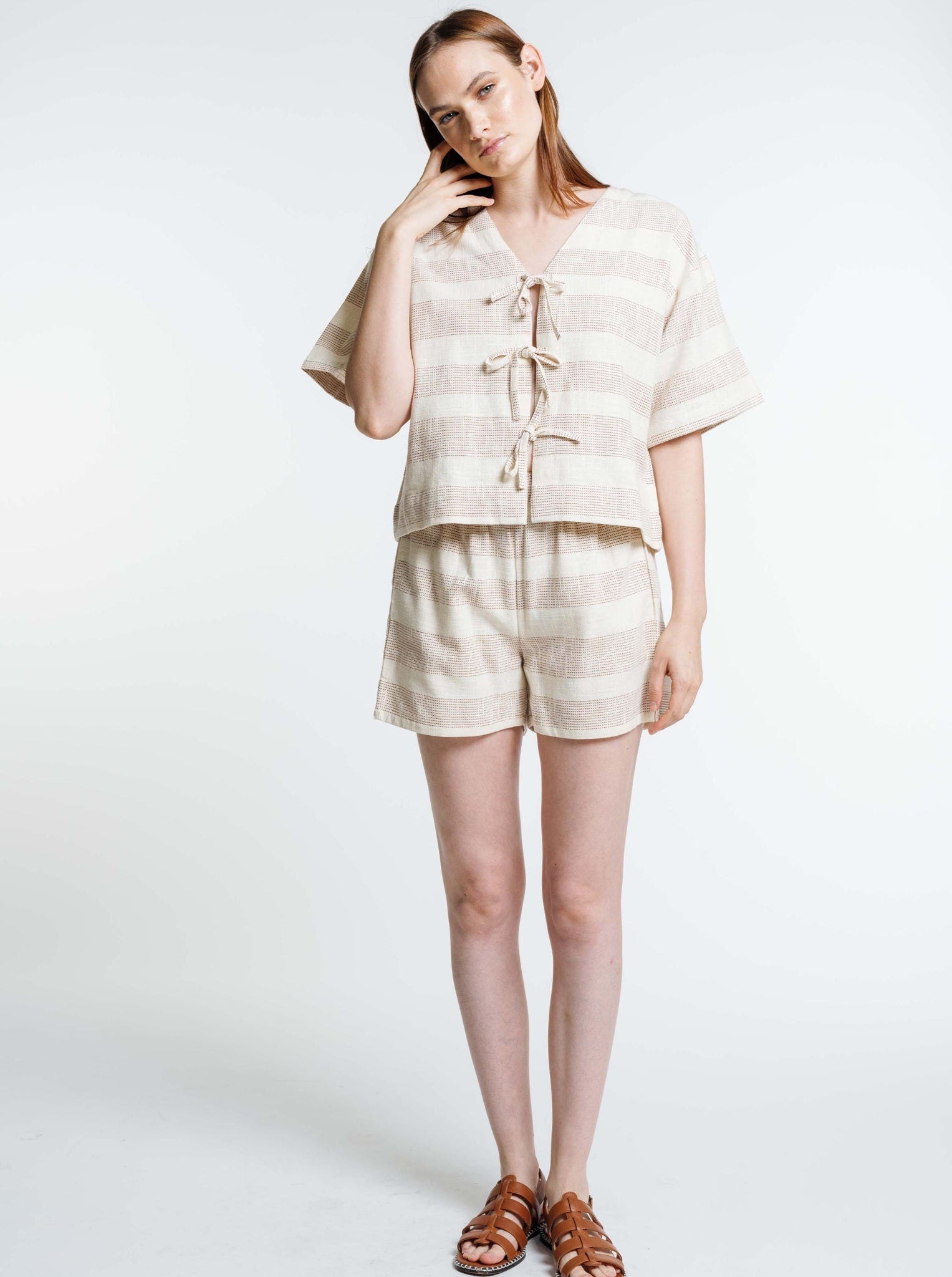 The model is wearing a Baker Top - Terracotta Ticking Stripe - Sample with short sleeves.