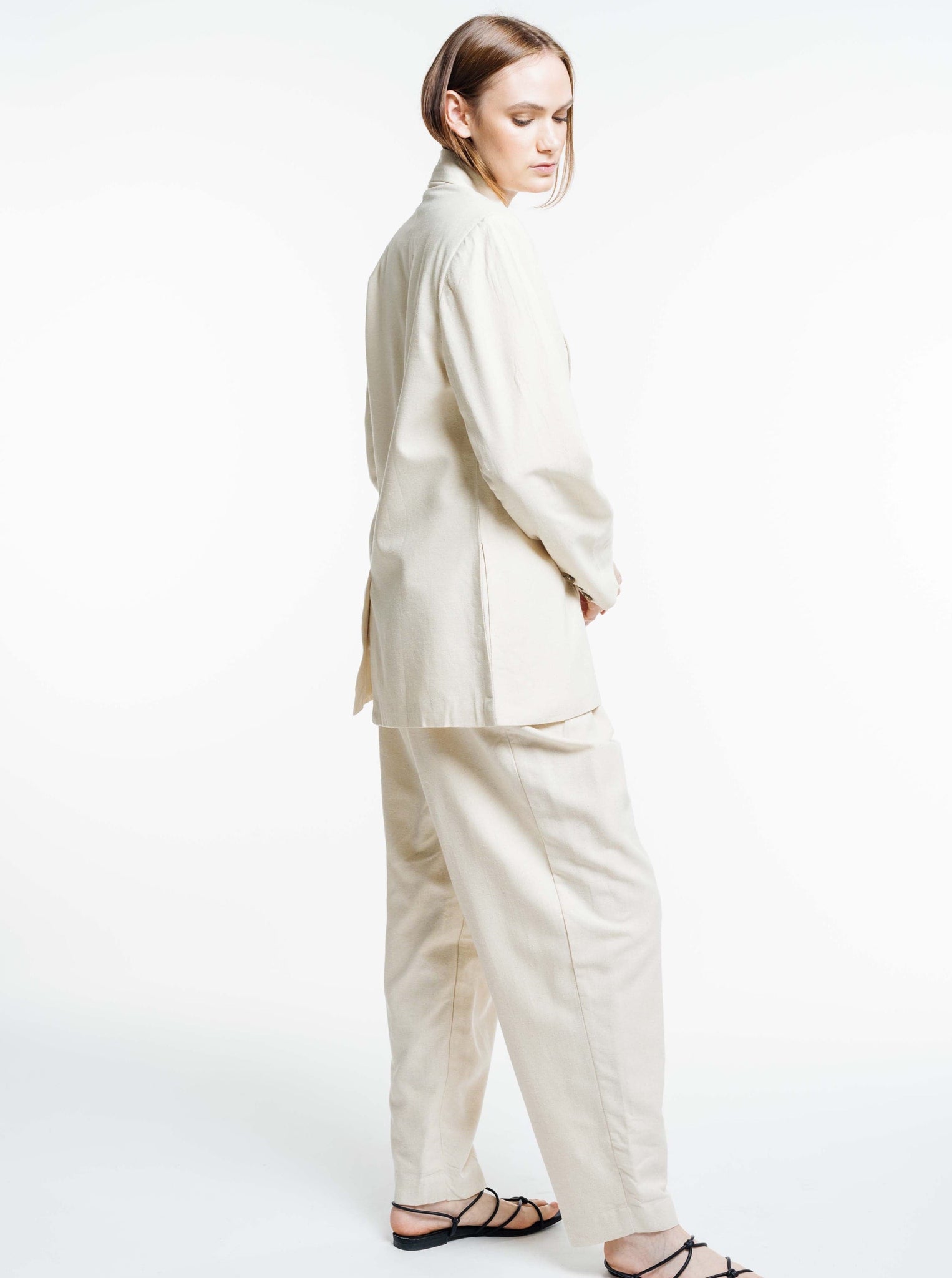 A woman in a white Bea Blazer - Ecru Silk Noil - Sample and sandals, inspired by menswear.
