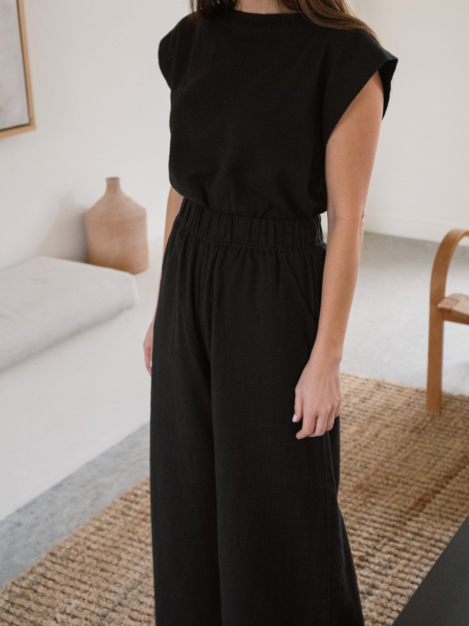 A woman standing in a living room wearing the Everyday Crop Pant - Black.