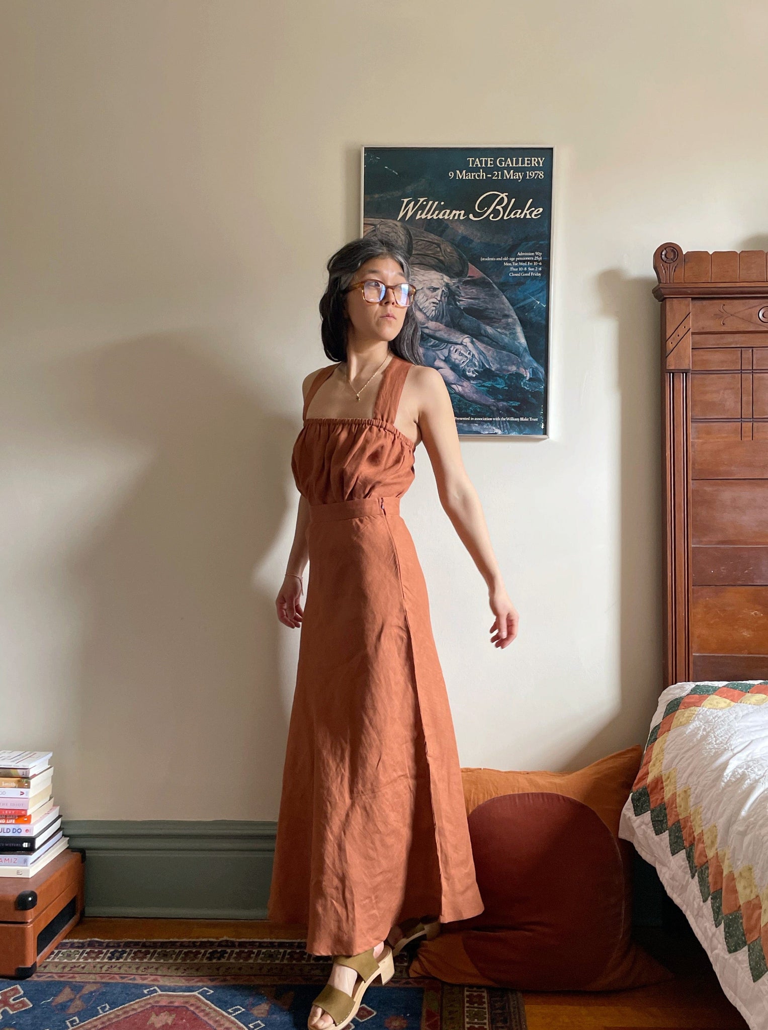 A woman in a Jardín Midi Skirt - Amber Brown - Sample standing in front of a bed.