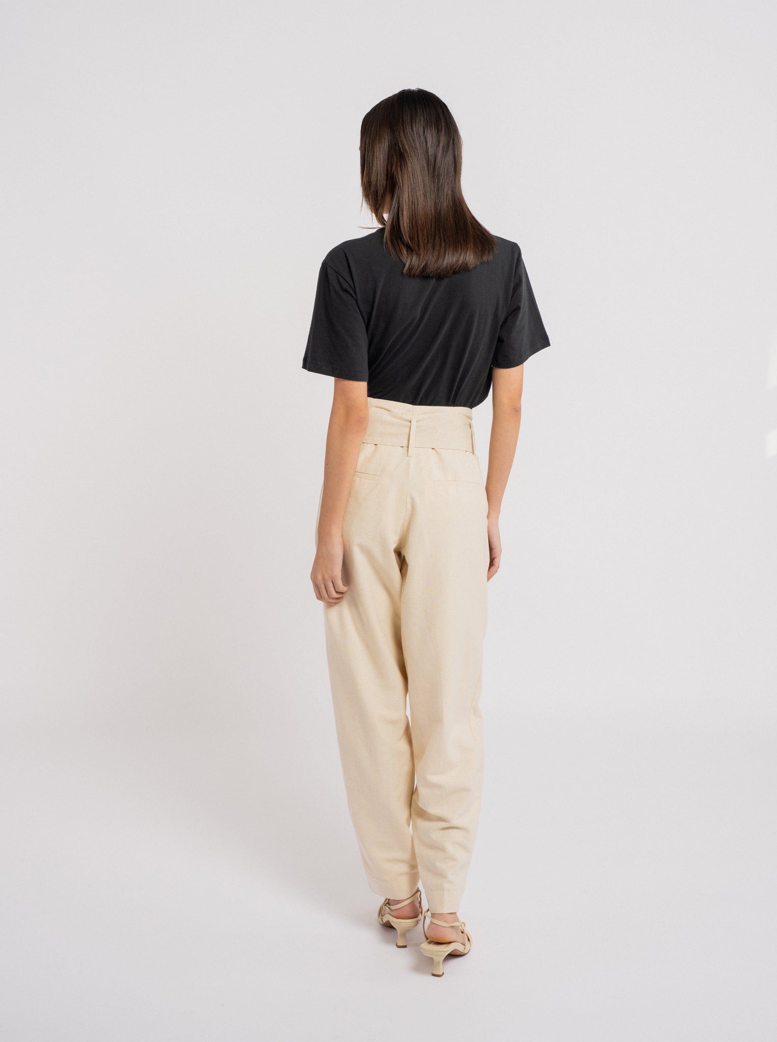 The back view of a woman wearing a Traveler Pant - Ecru Silk Noil - Sample and beige trousers.